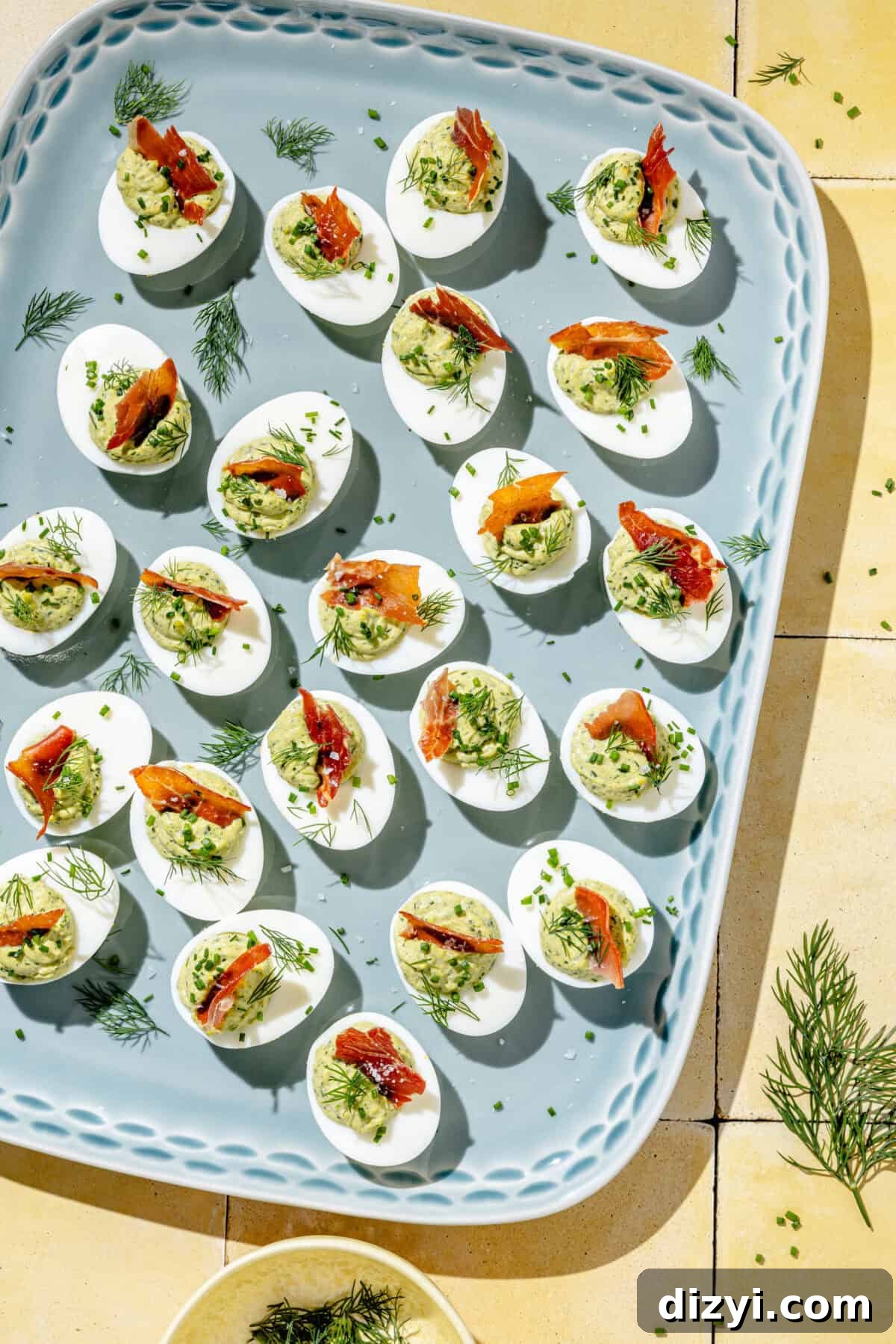 a platter of green goddess deviled eggs topped with pancetta and fresh dill