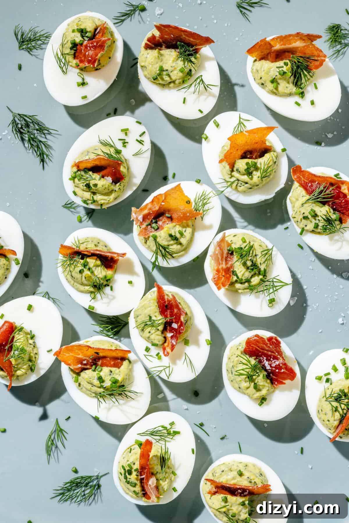 green goddess deviled eggs topped with fresh dill and pancetta on a light blue background