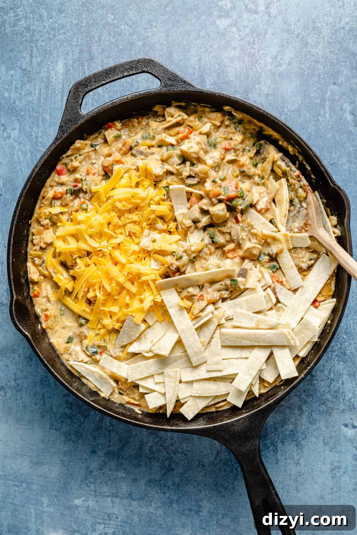 a cast-iron skillet with king ranch chicken casserole topped with shredded cheddar cheese and corn tortilla strips on a blue background