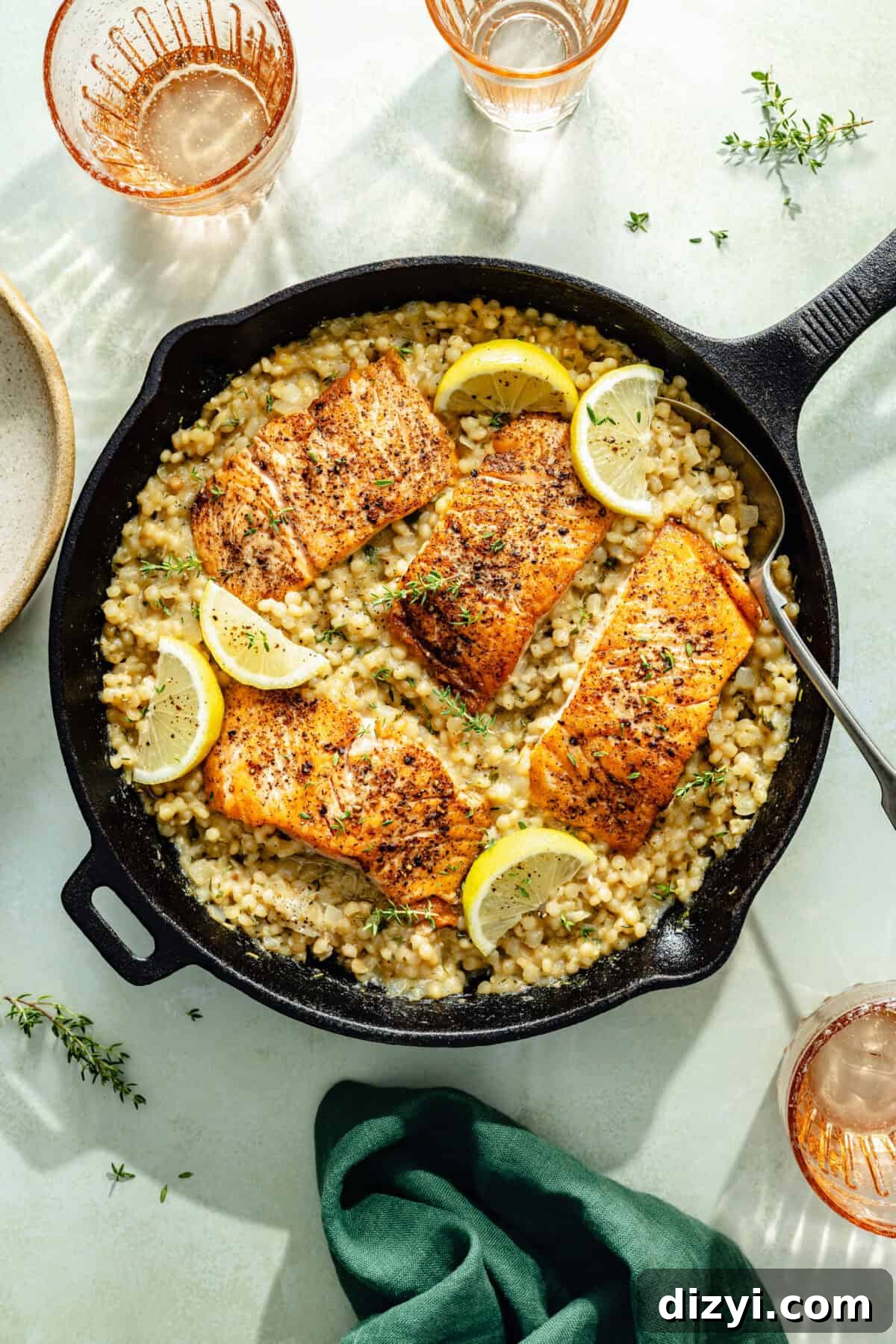 One-Pan Salmon with Herbed Butter Couscous 2 a cast-iron skillet with herby Israeli couscous, seared salmon, and lemon wedges