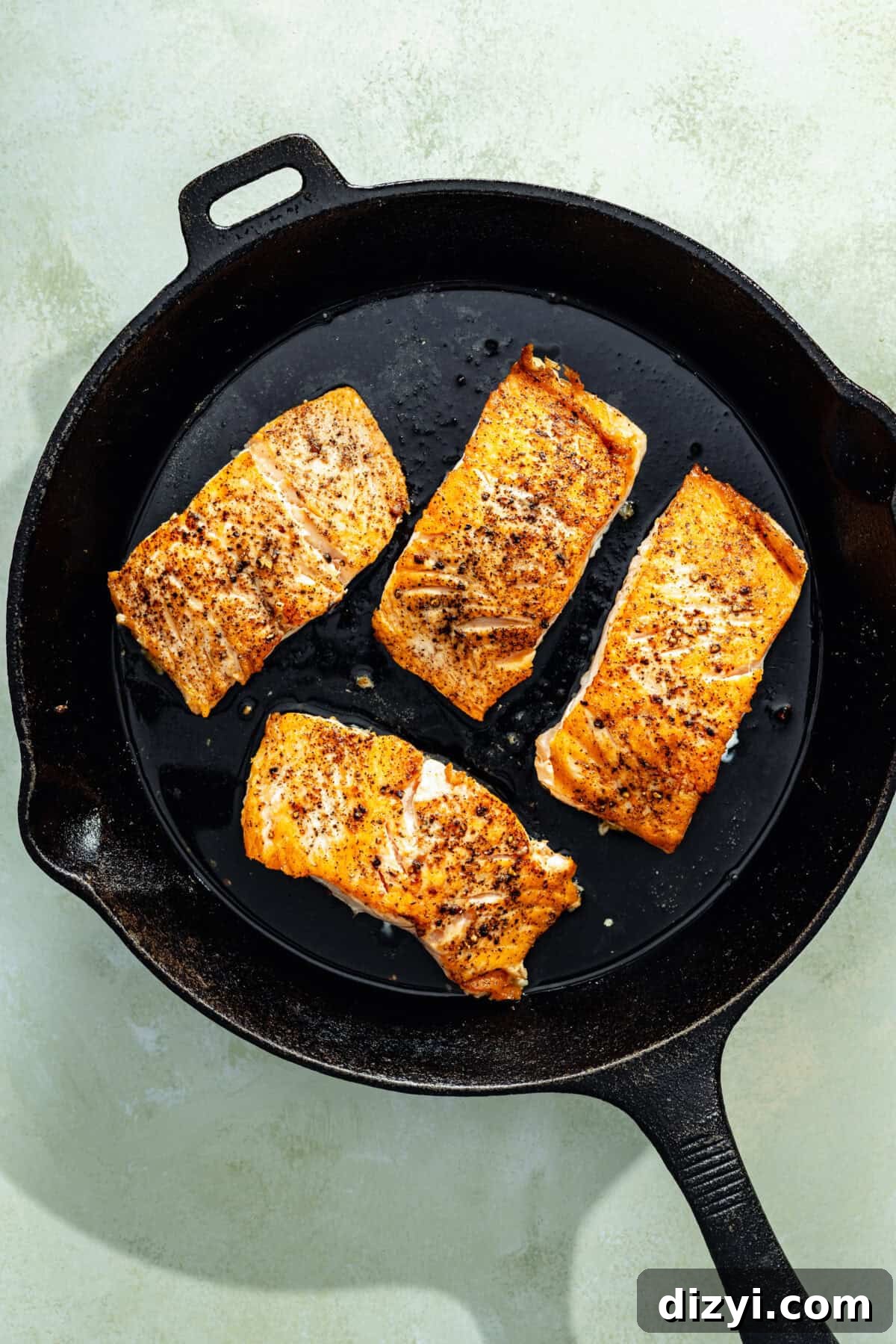One-Pan Salmon with Herbed Butter Couscous 3 a cast-iron skillet with seasoned seared salmon on a light green background
