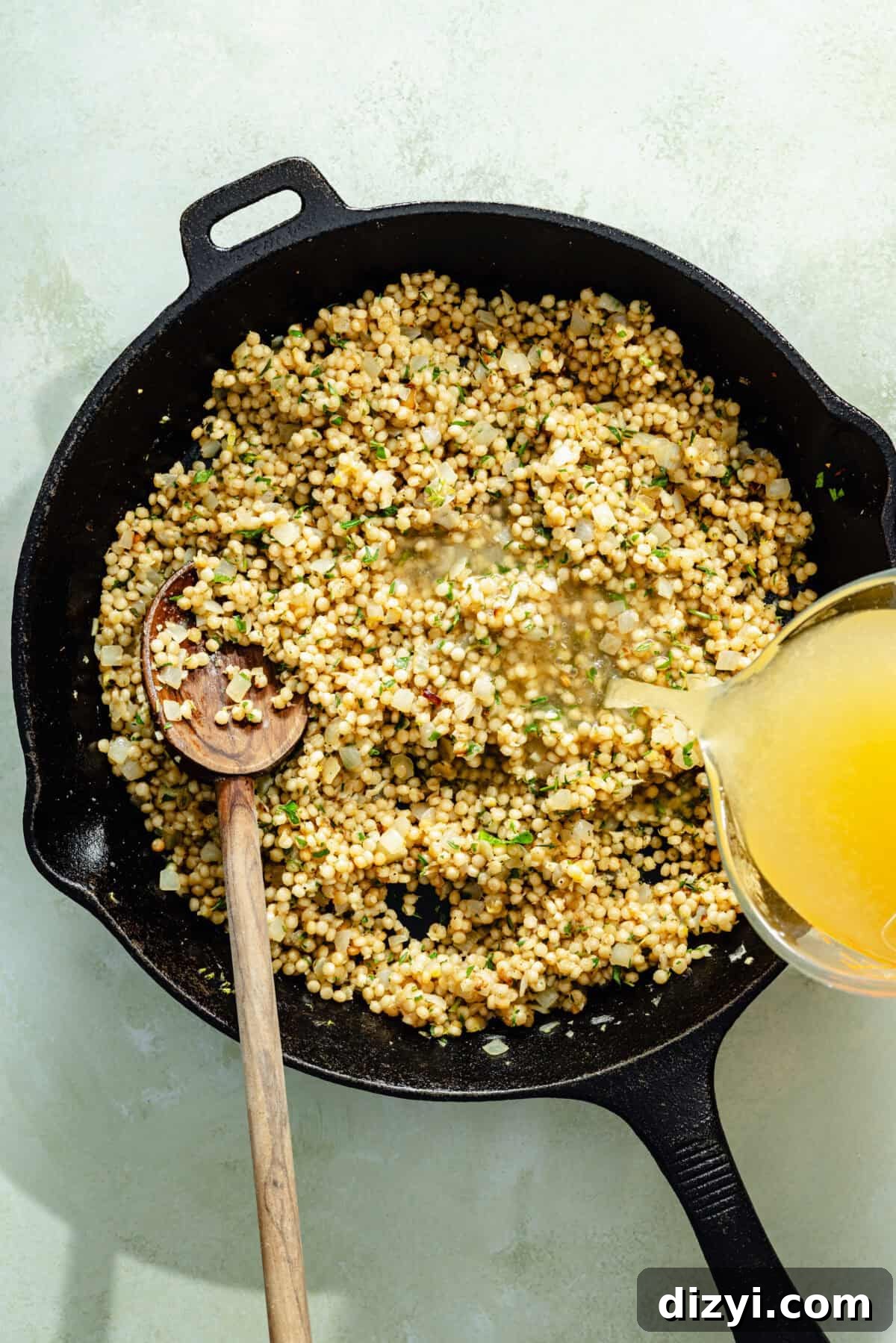 One-Pan Salmon with Herbed Butter Couscous 4 a cast-iron skillet with herby couscous and chicken broth on a light green background