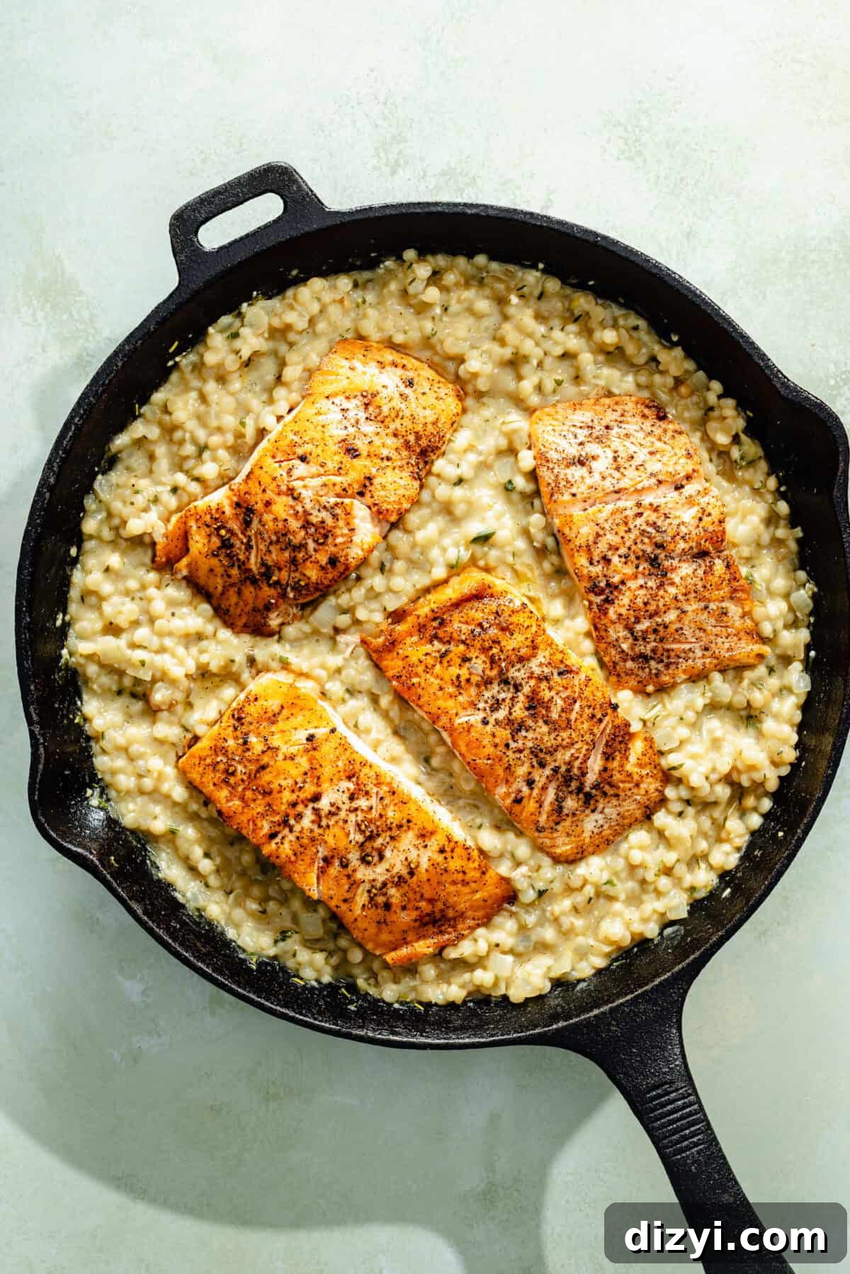 One-Pan Salmon with Herbed Butter Couscous 5 seared salmon nestled in herby couscous in a cast-iron skillet on a light green background