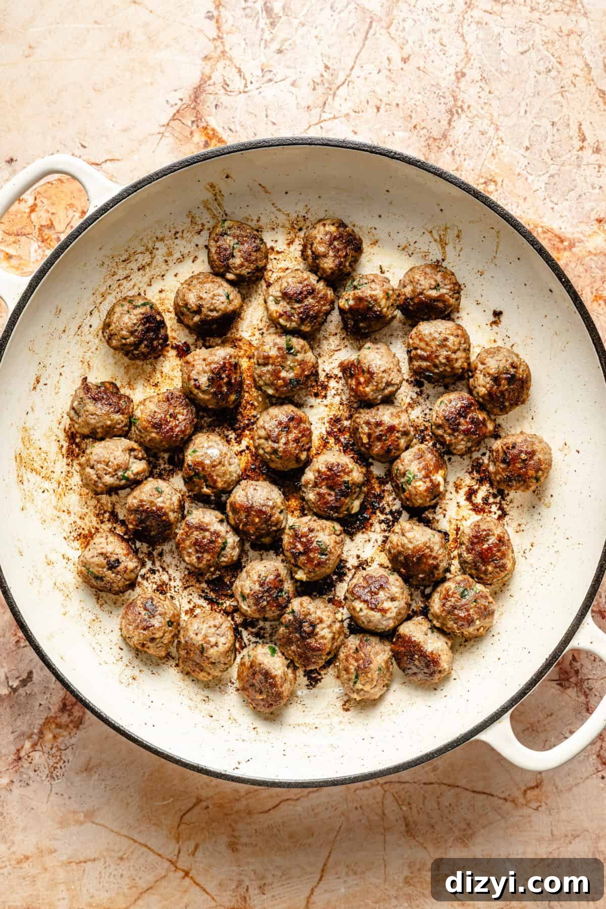 a white cast-iron braiser with cooked mini meatballs