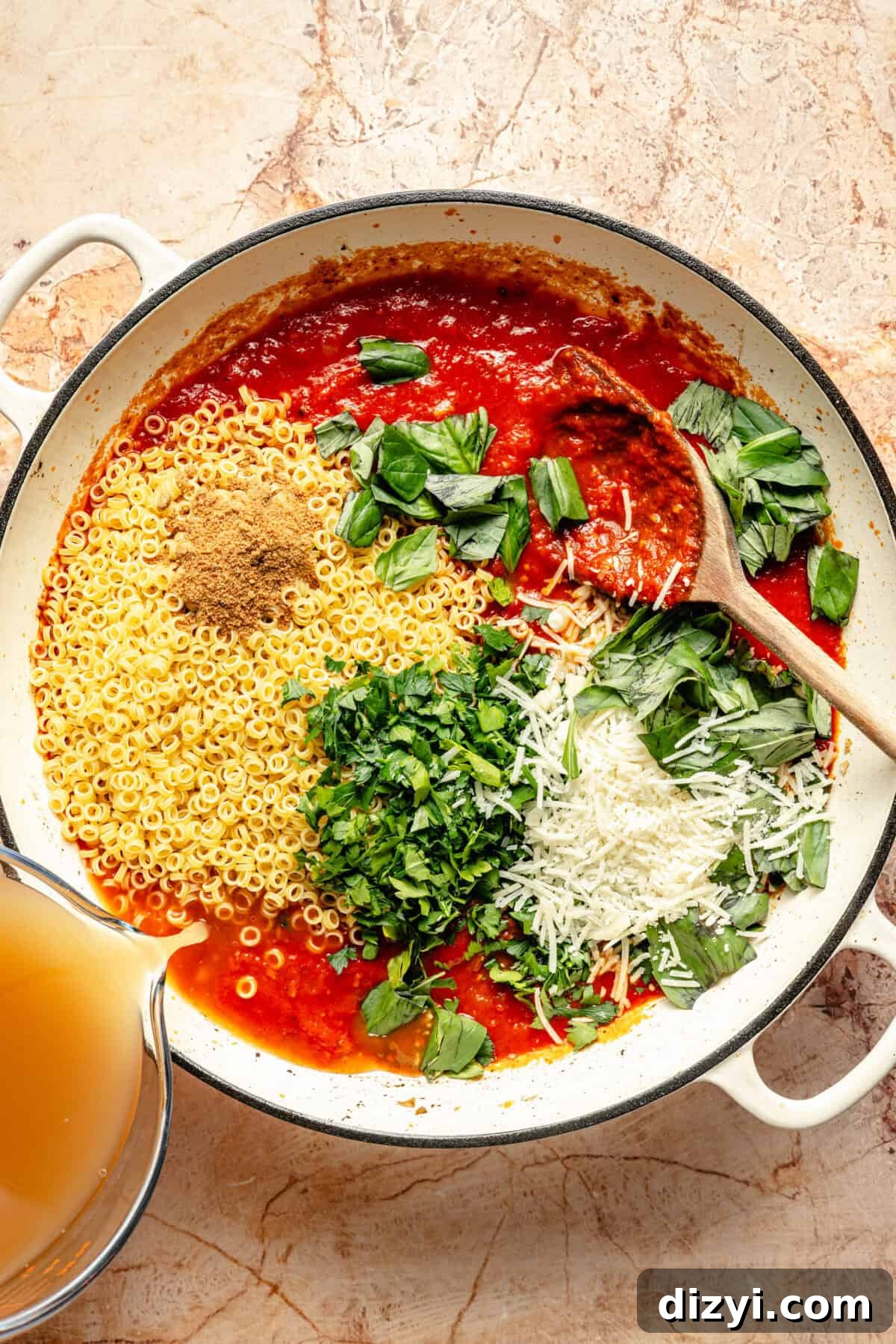 a cast-iron braiser with marinara sauce, fresh herbs, grated cheese, and pasta