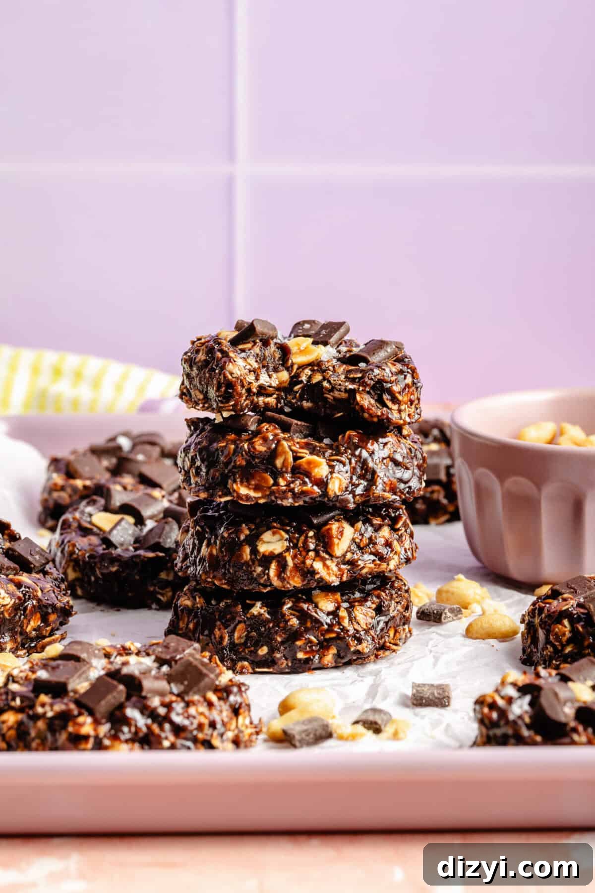 No-Bake Chocolate Peanut Butter Cookies Recipe 5 a stack of chocolate and oat cookies with salted peanuts on a light purple background