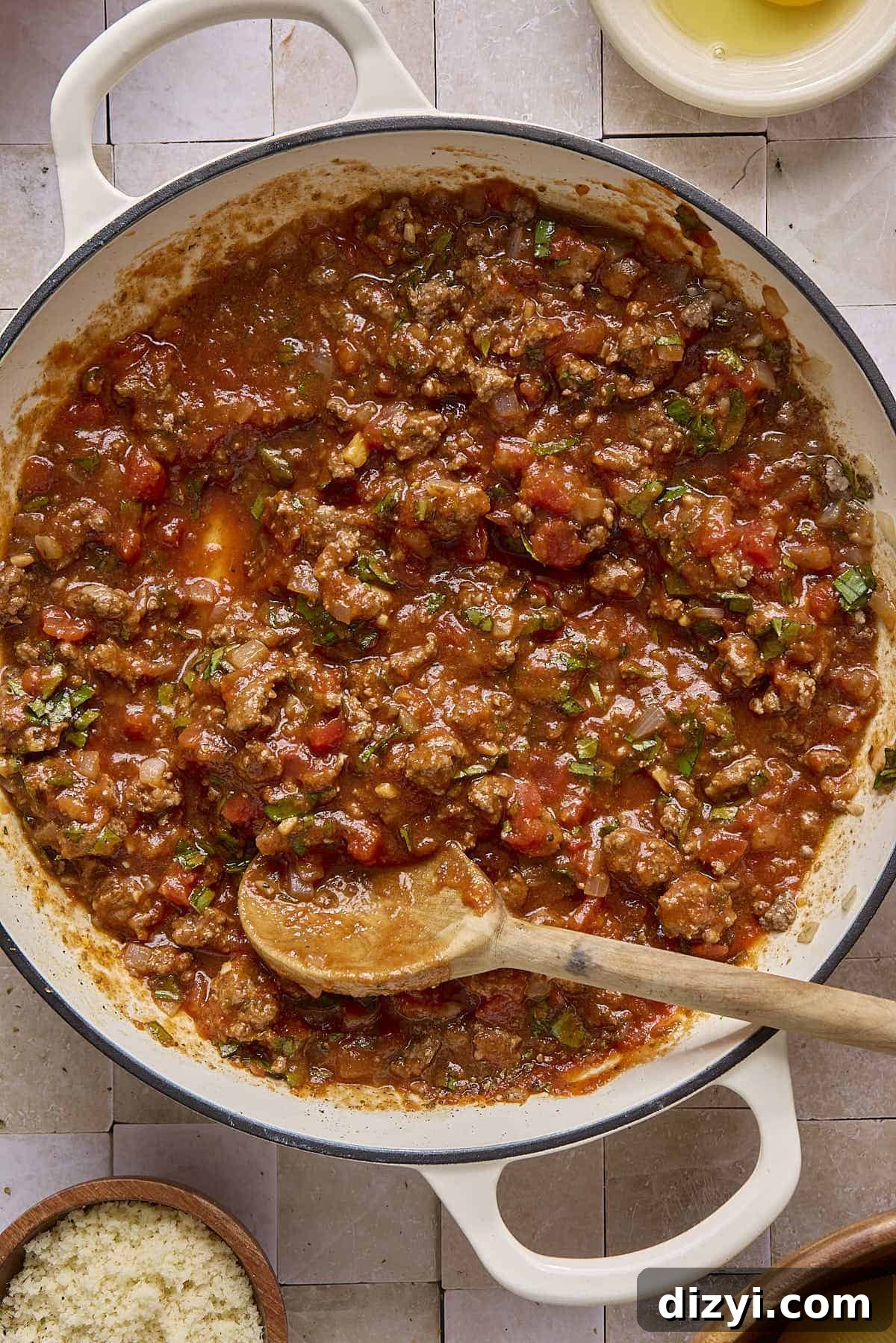 a white cast-iron braiser with ground beef and marinara sauce