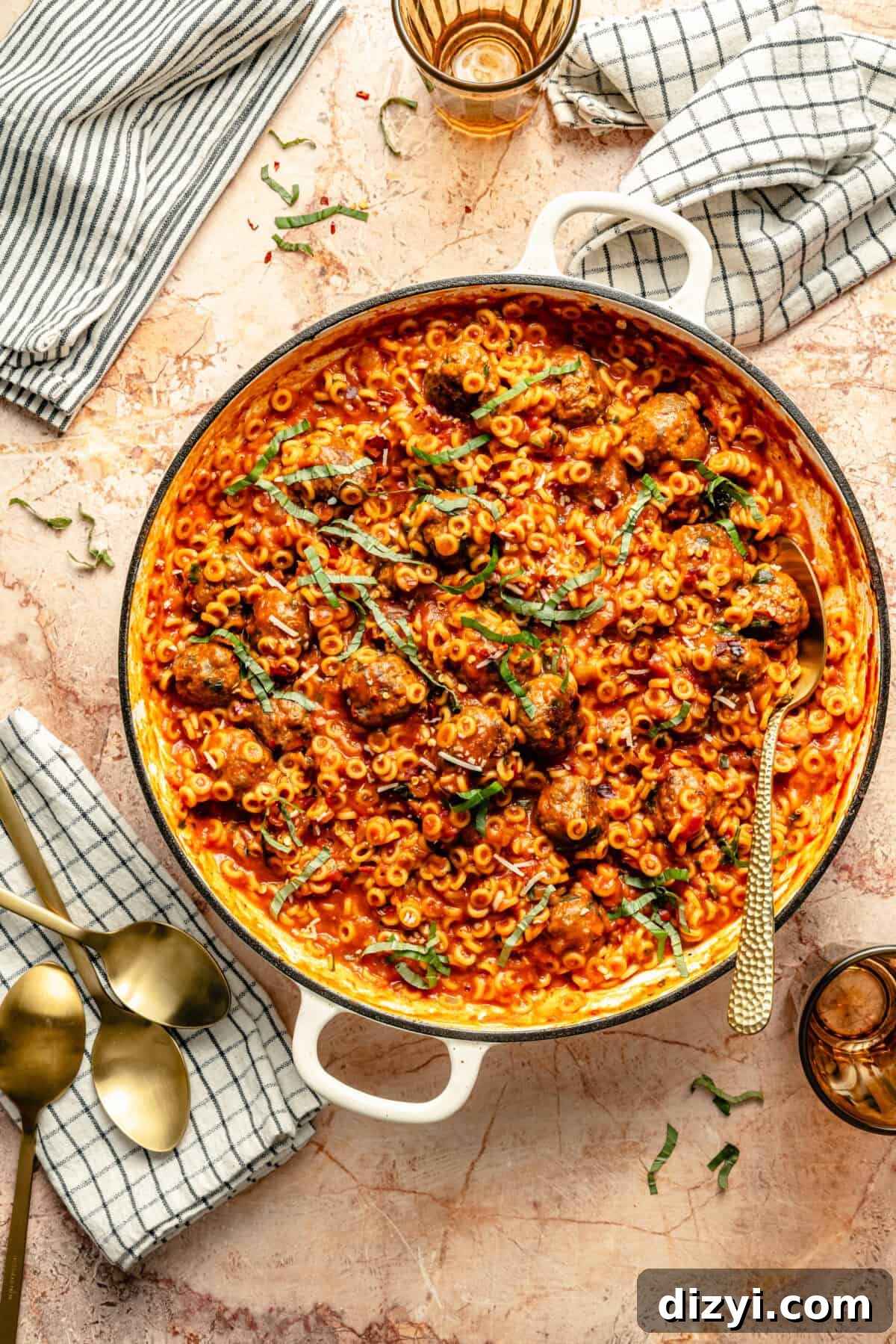 a large braiser with meatballs and spaghetti-o's with fresh herbs and a dishcloth