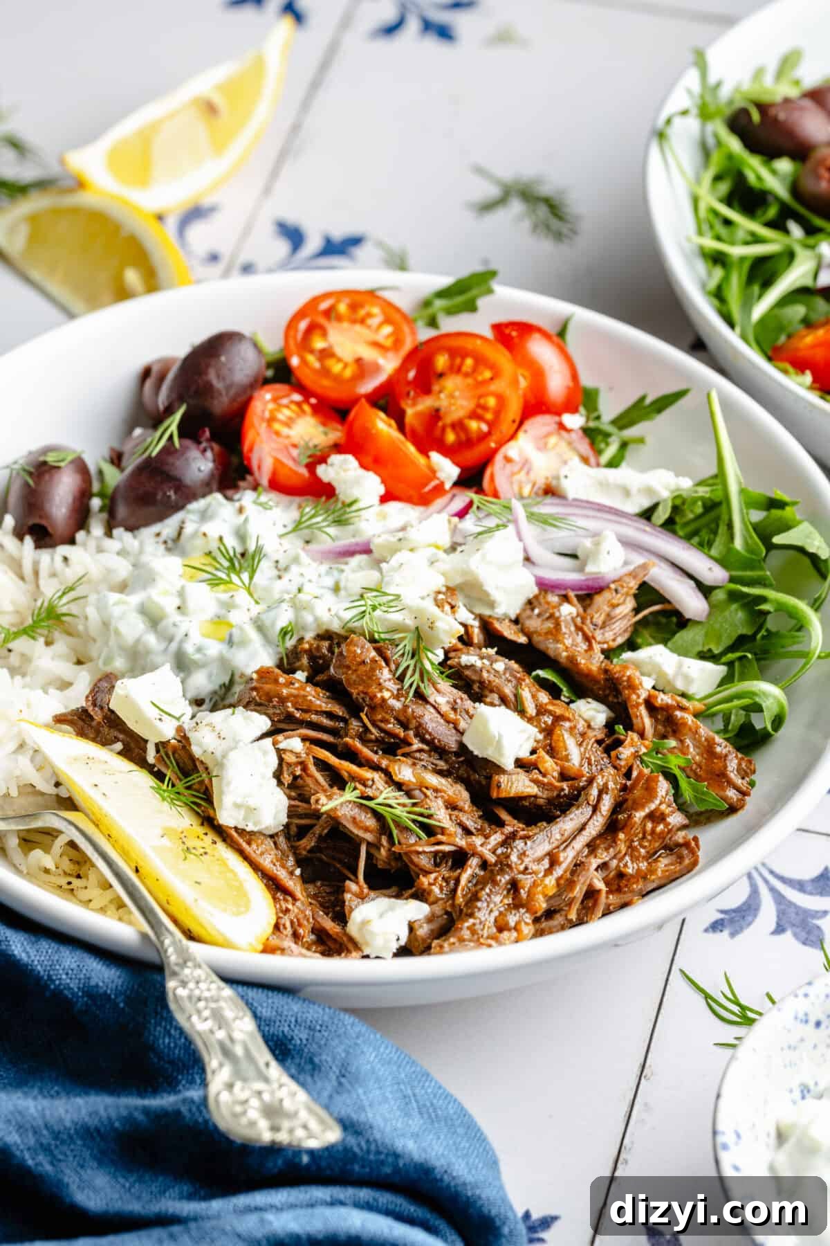 Instant Pot Shredded Greek Beef in bowl with garnishes scattered around.