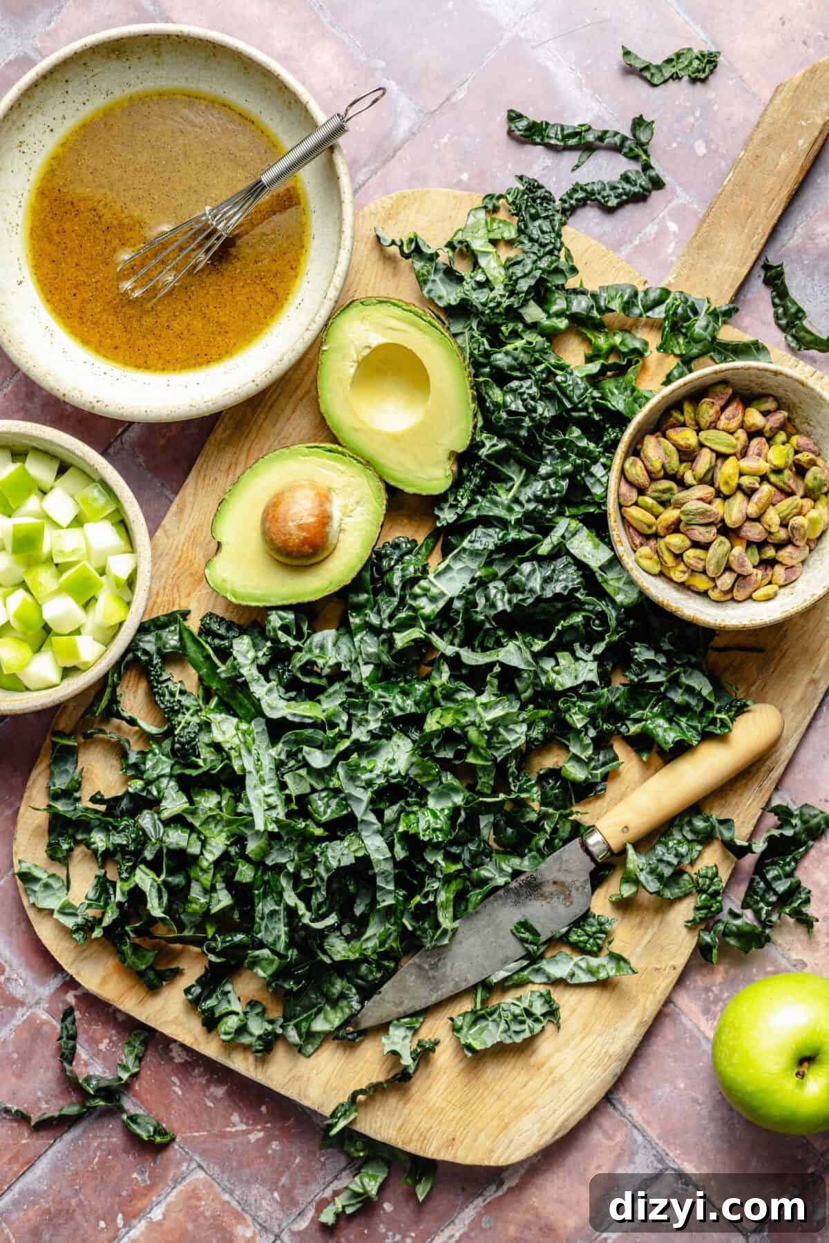 Citrus Kale Detox Salad with Lemon Ginger Dressing 3 a wooden cutting board with shredded kale, fresh avocado, pistachios, and green apple on a light brick background