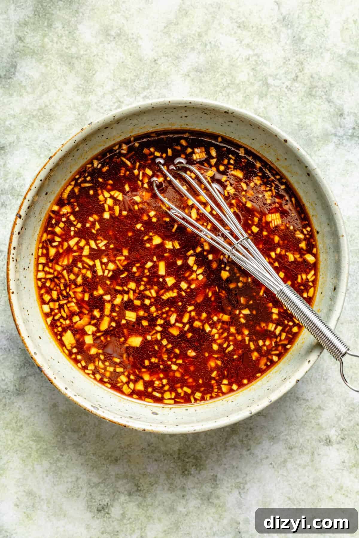 a shallow bowl of a spicy Sriracha sauce with a small stainless steel whisk