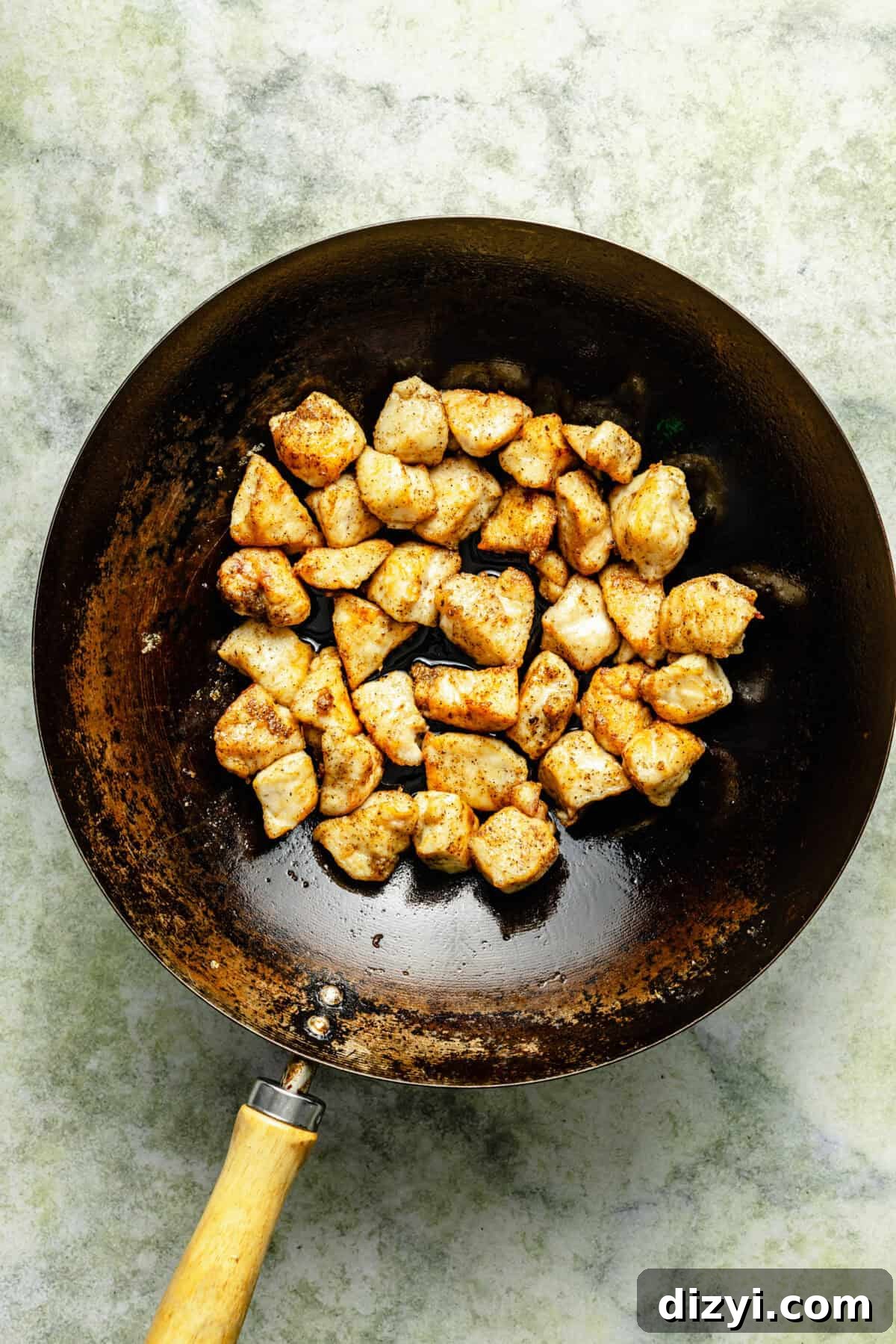 cubed and cooked chicken in a dark skillet on a light green background
