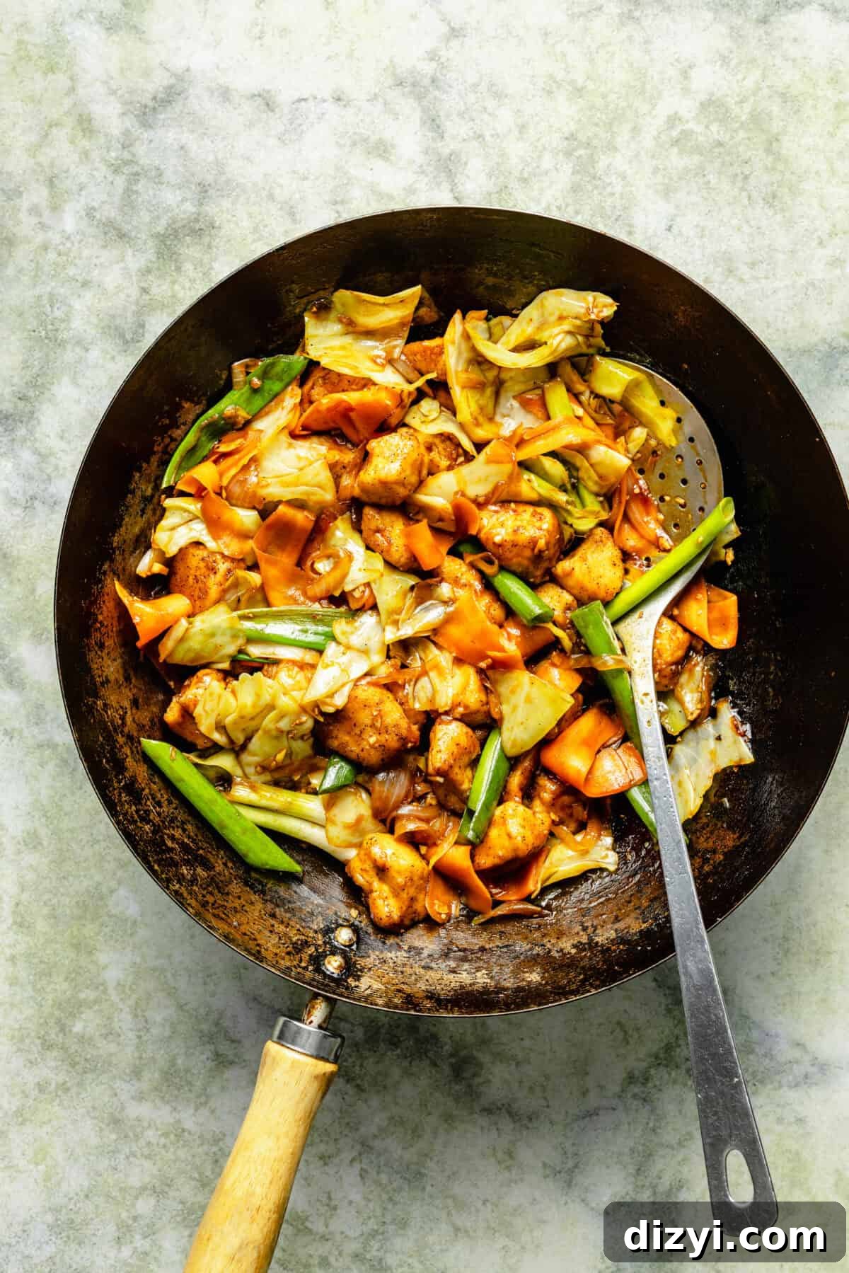 a dark skillet with chicken and vegetables, along with a long stainless steel spoon