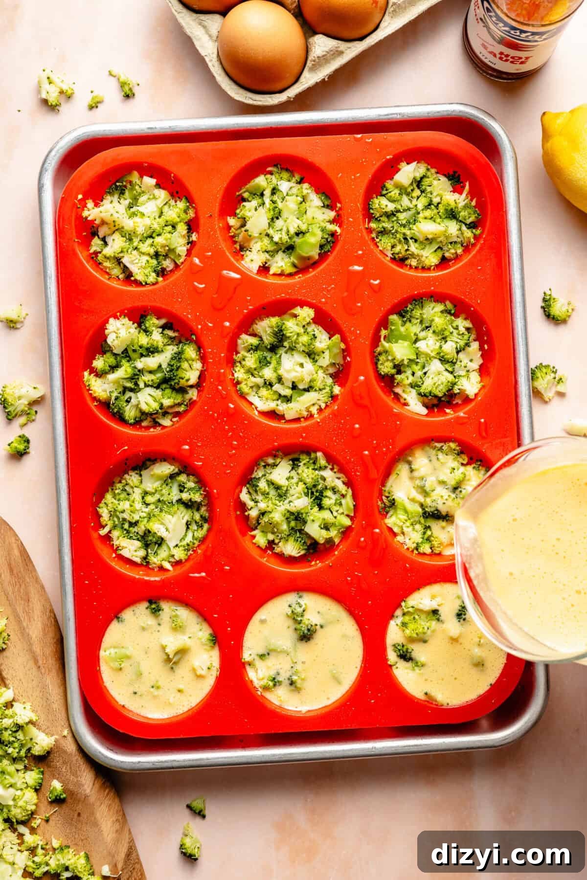a red silicone muffin tin with unbaked broccoli egg cups and lemon