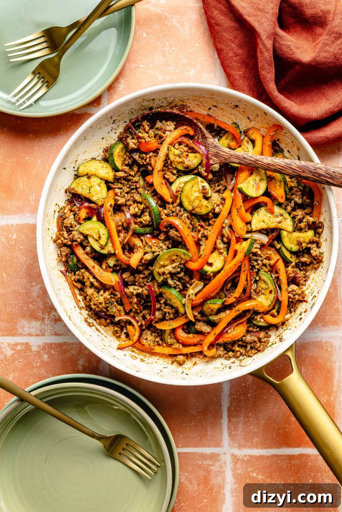 One-Pan Mediterranean Beef and Vegetable Skillet Recipe 5 a white and gold skillet with ground beef and sautéed vegetables with green plates and gold forks on the side