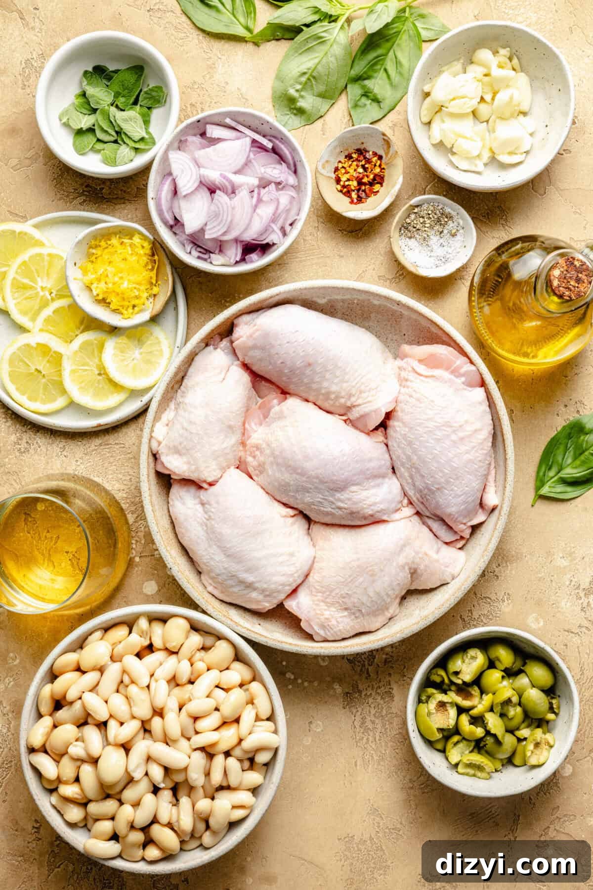 raw chicken thighs with white beans, olives, lemons, onions, and herbs on a tan background