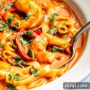 a close-up of gochujang and coconut shrimp noodle soup with herbs in a white bowl