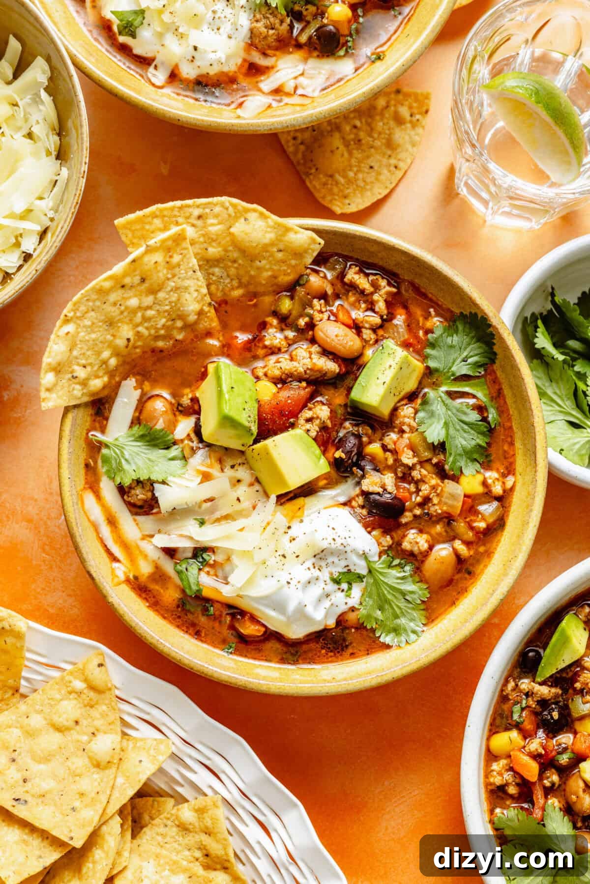 Turkey Taco Soup with Black Beans and Corn 5 a large yellow bowl filled with turkey taco soup topped with diced avocado, sour cream, and tortilla chips on an orange background