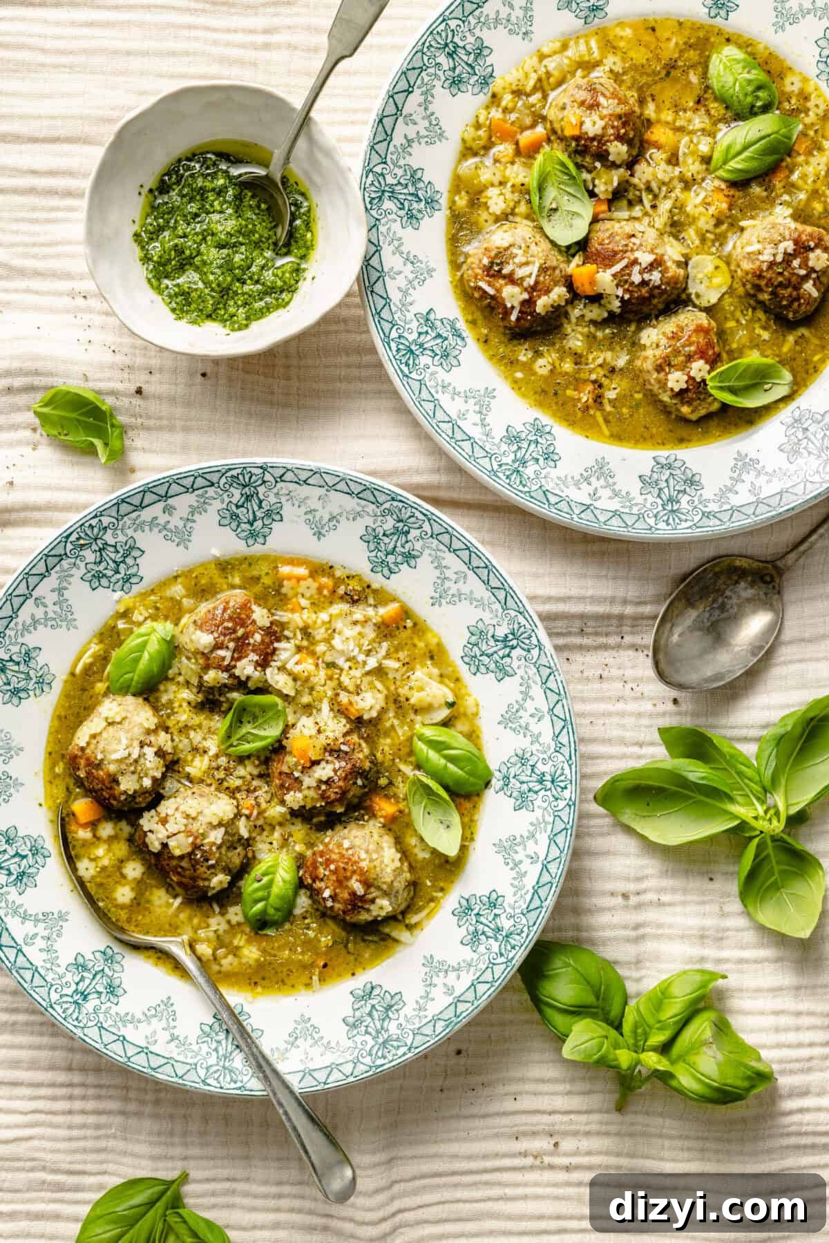 two green and white toile bowls filled with pesto meatball and pastina soup; garnished with fresh basil leaves