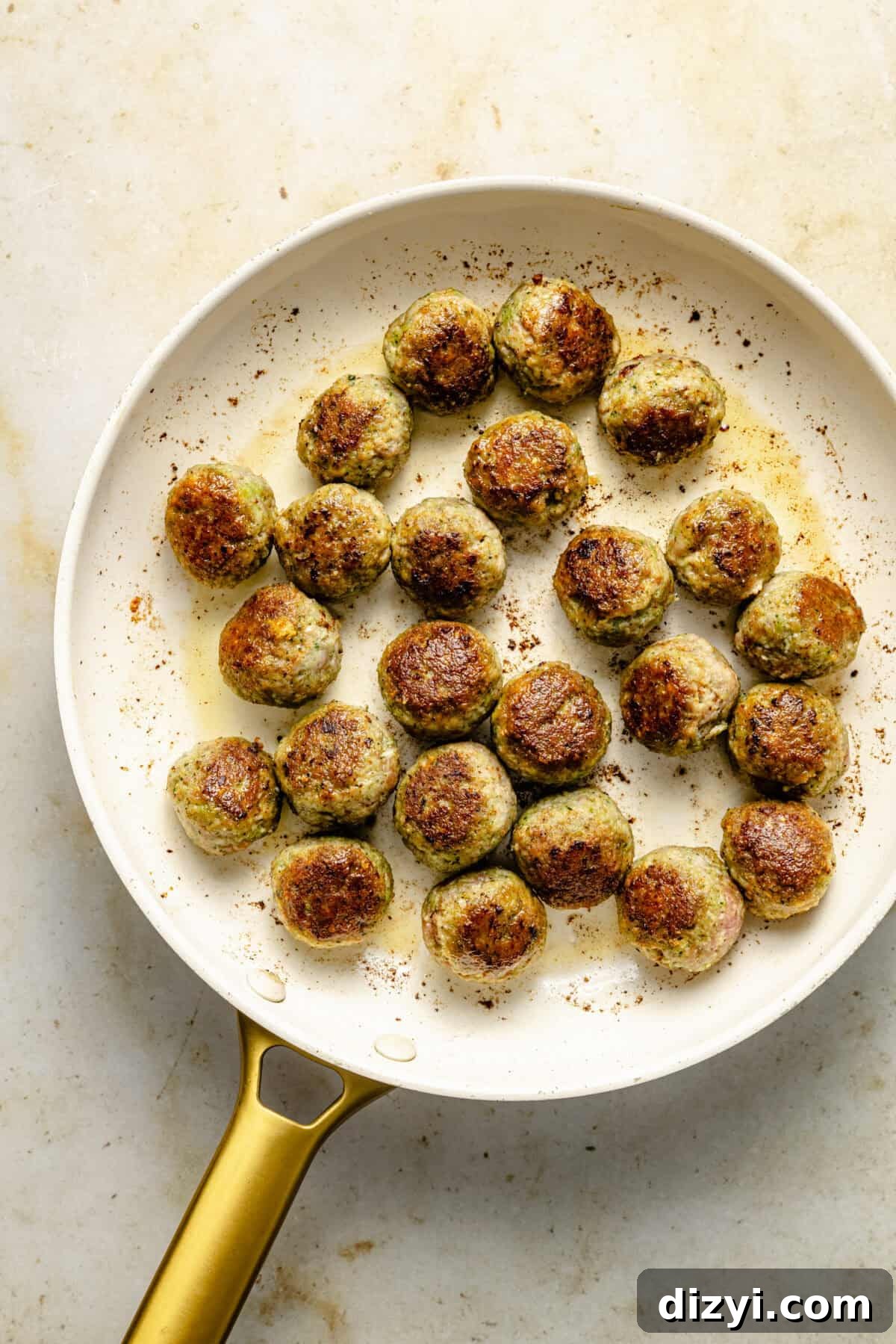 a white skillet with seared pesto meatballs on a neutral background