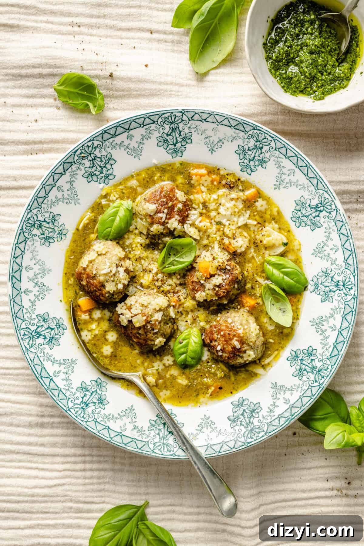 a green and white toile patterned bowl filled with pesto meatballs and pasta soup
