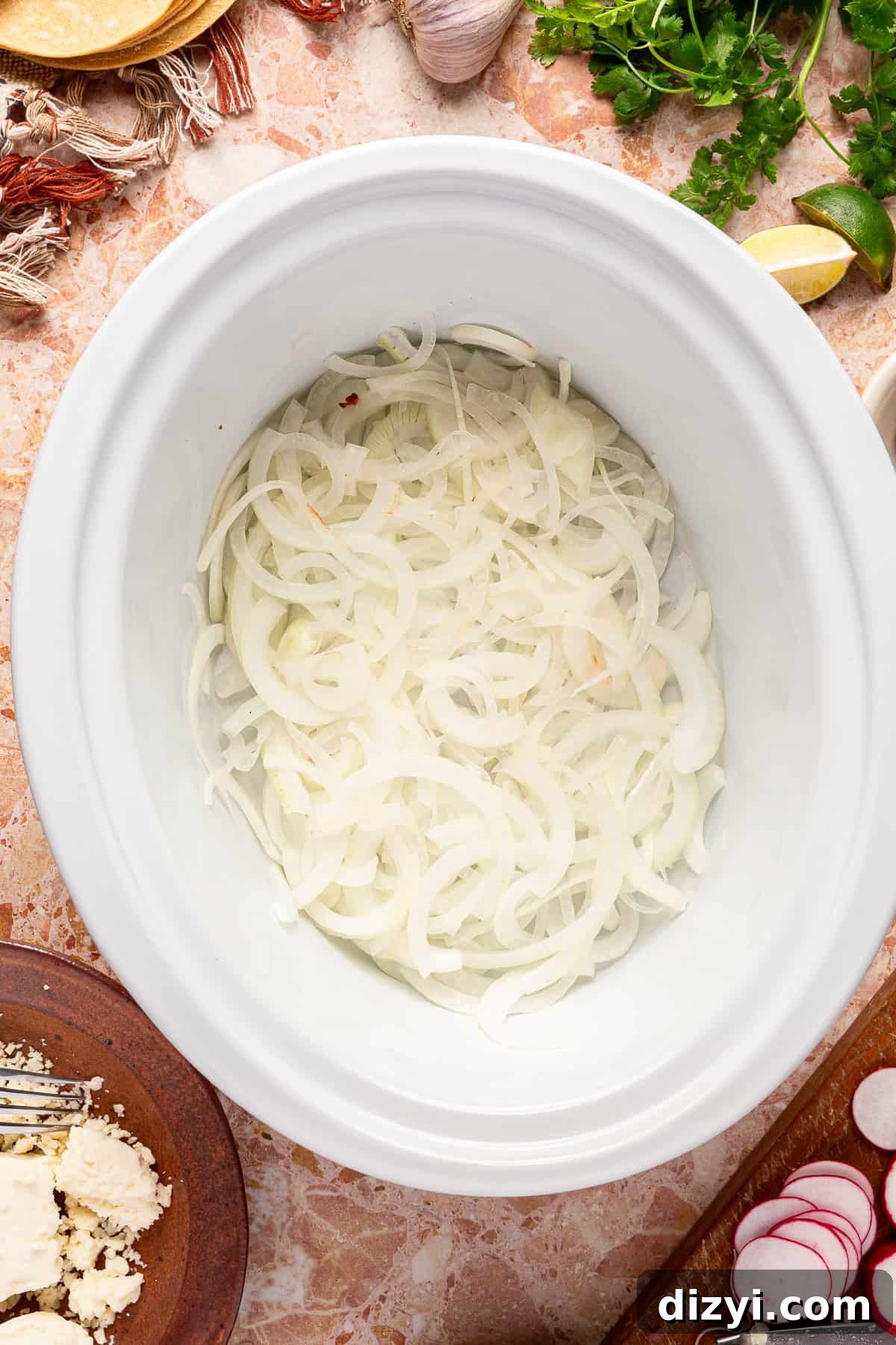A layer of thinly sliced white onions on the bottom of a crockpot.