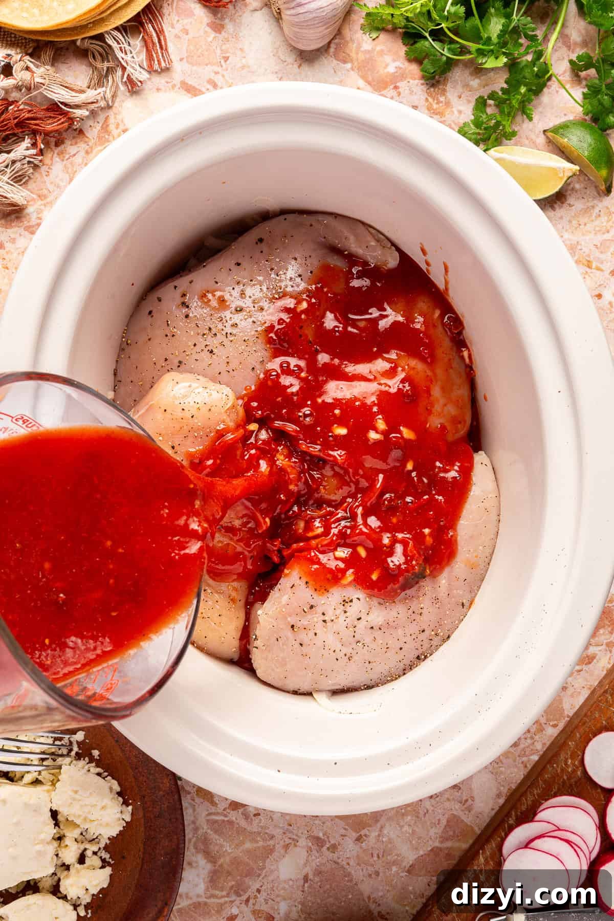 The chicken tinga taco sauce being poured over the chicken breasts in the crockpot.