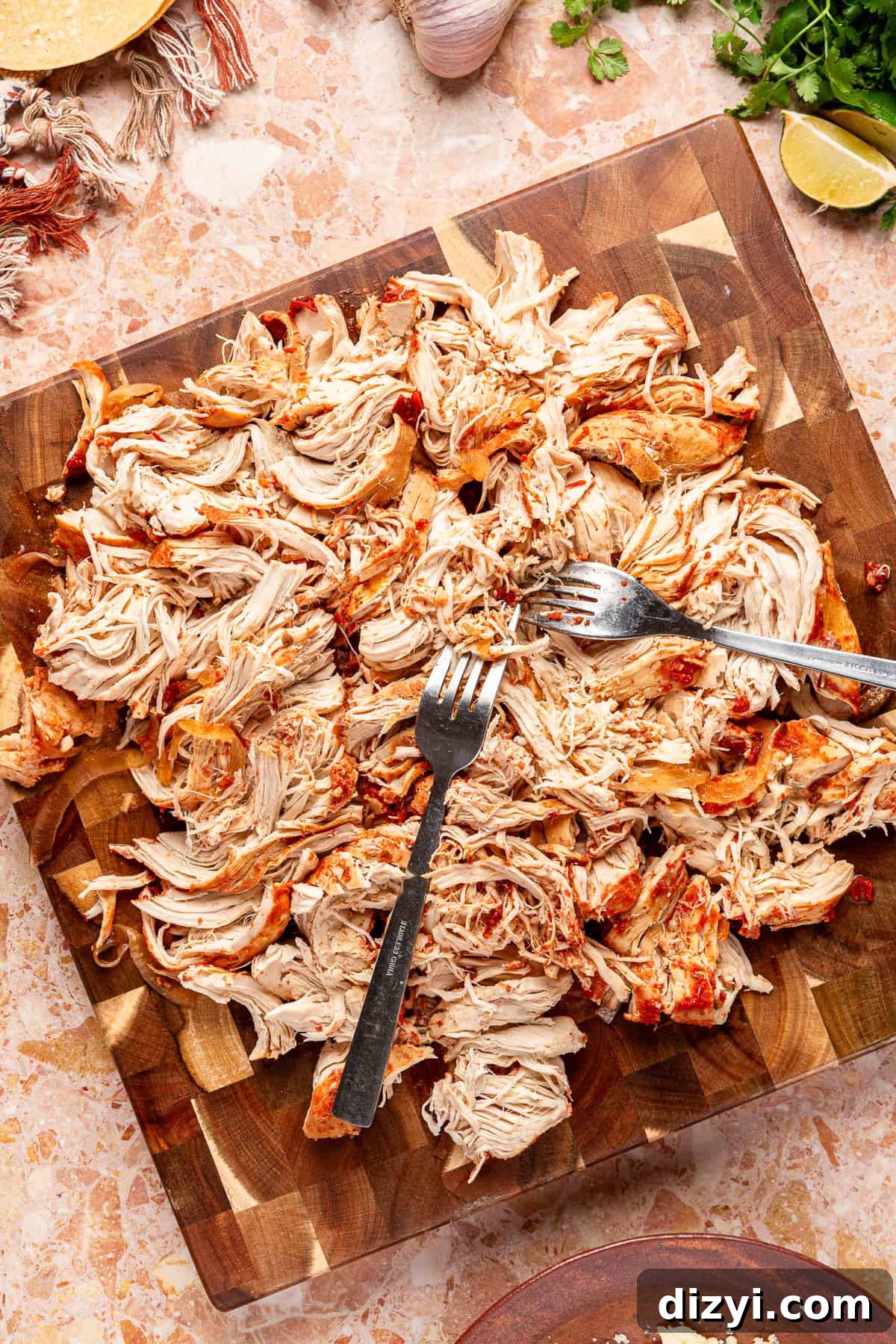 Two forks being used to shred chicken on a cutting board.