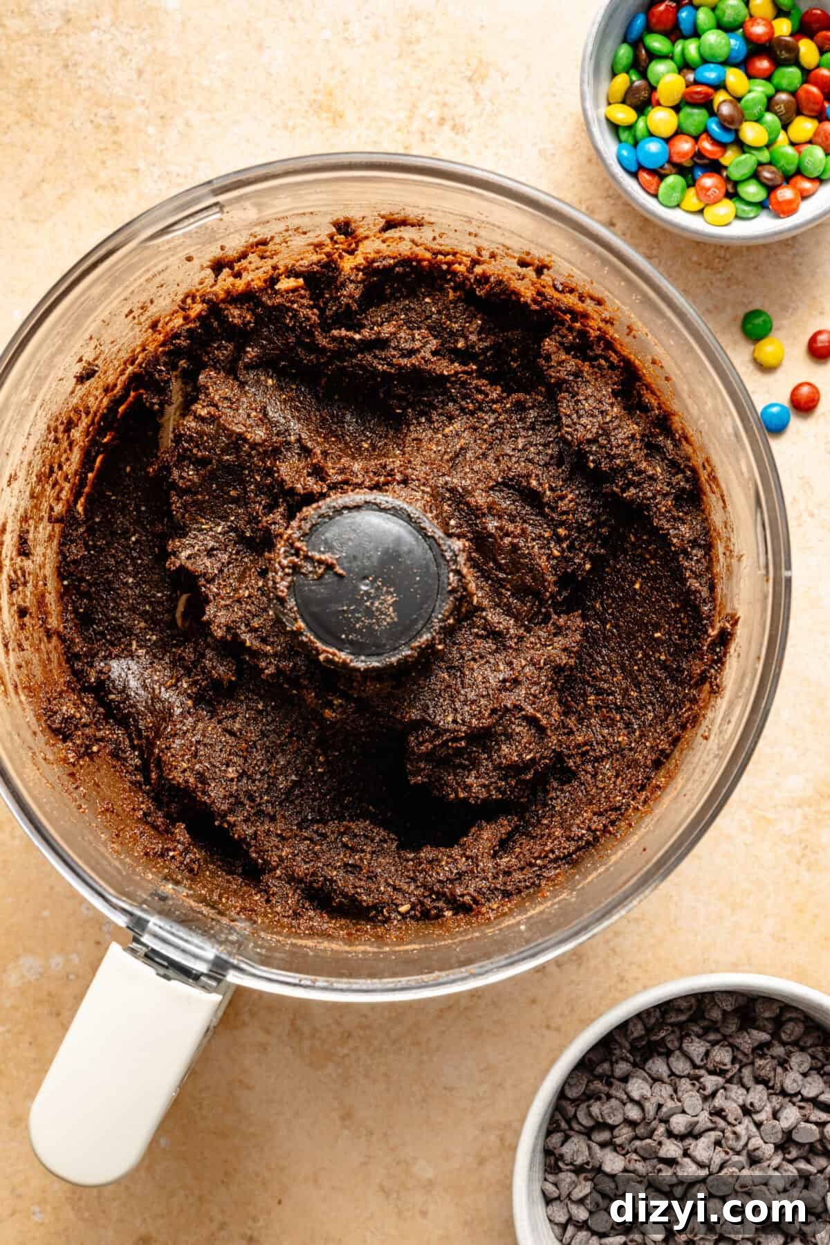 Cosmic Brownie Energy Bites Recipe - No-Bake Chocolate Snack 5 a food processor filled with a mixture of brownie energy bites; a small side bowl of mini M&Ms and mini chooclate chips