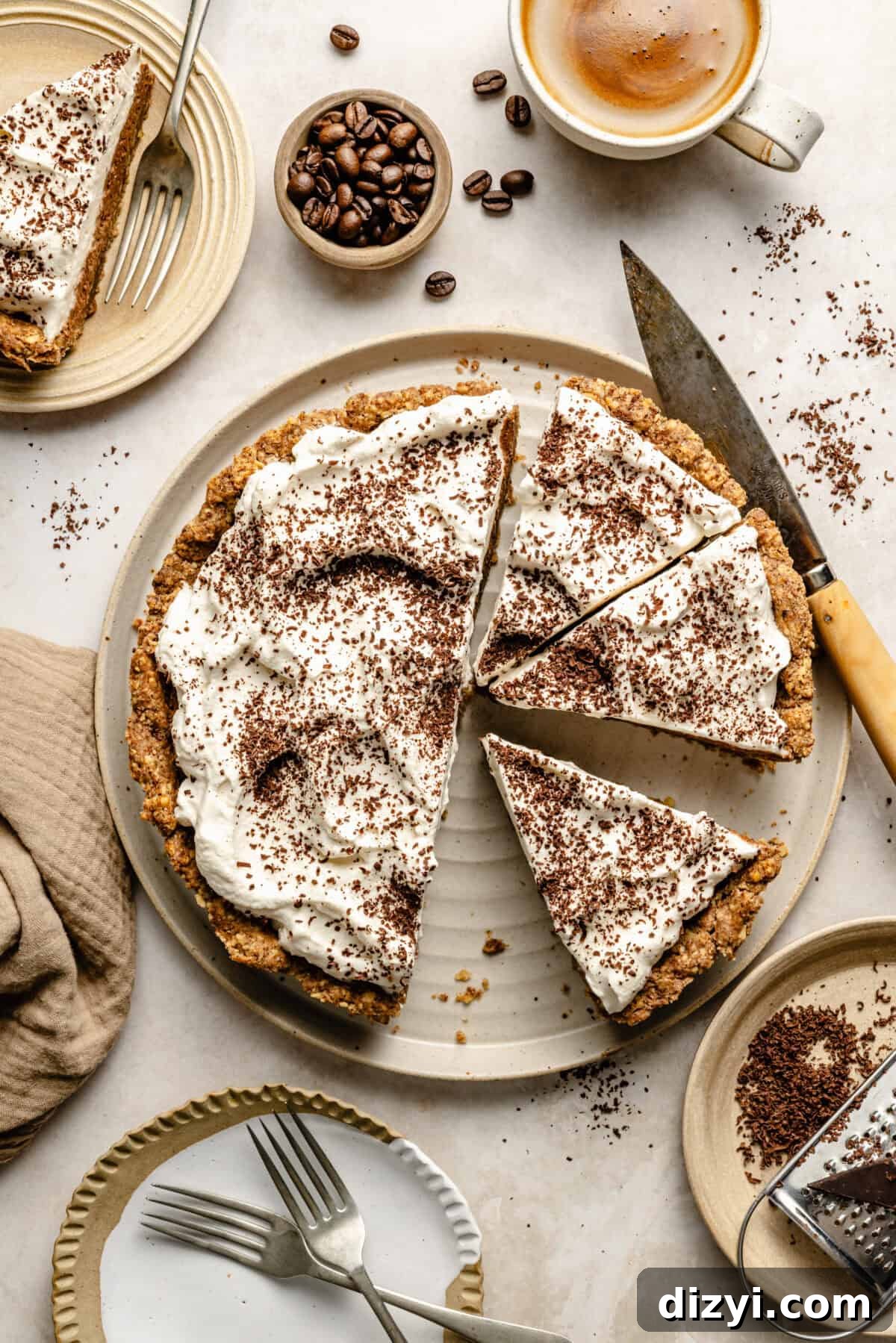 a coffee toffee pie topped with whipped cream and chocolate shavings on a neutral-colored plate; a small bowl of whole coffee beans is in the background