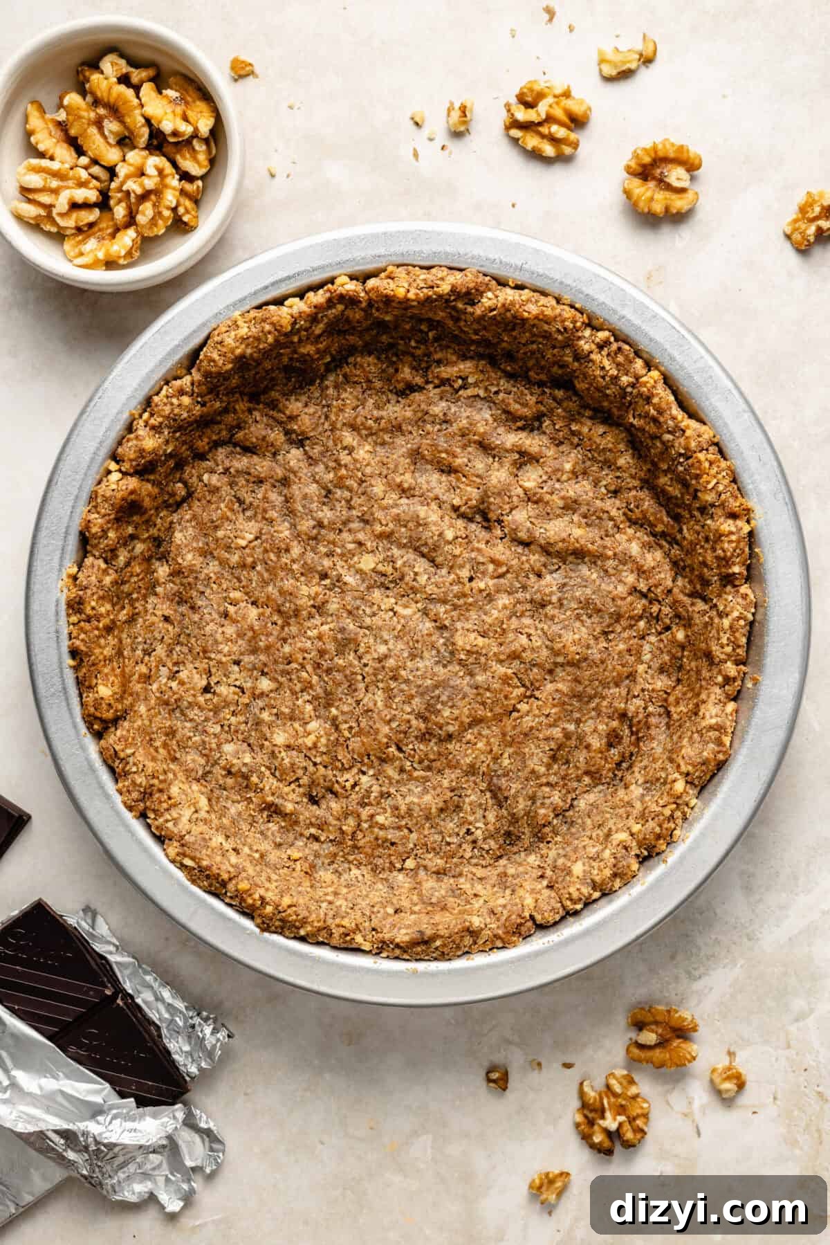 a chocolate and walnut pie crust in a metal baking dish on a neutral background