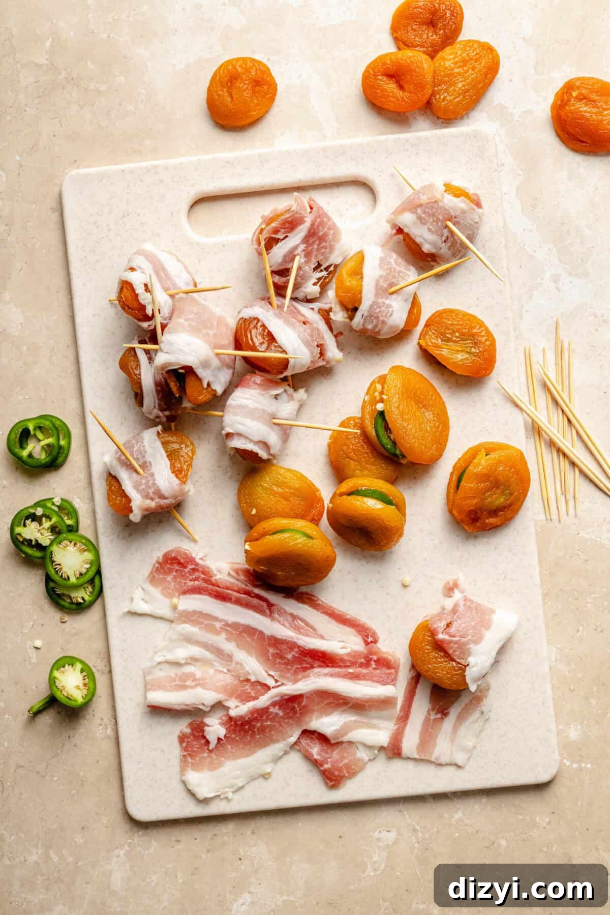 Bacon Wrapped Apricot Bites with Blue Cheese Drizzle 3 a white cutting board on a neutral background featuring jalapeño-stuffed apricots and slices of bacon