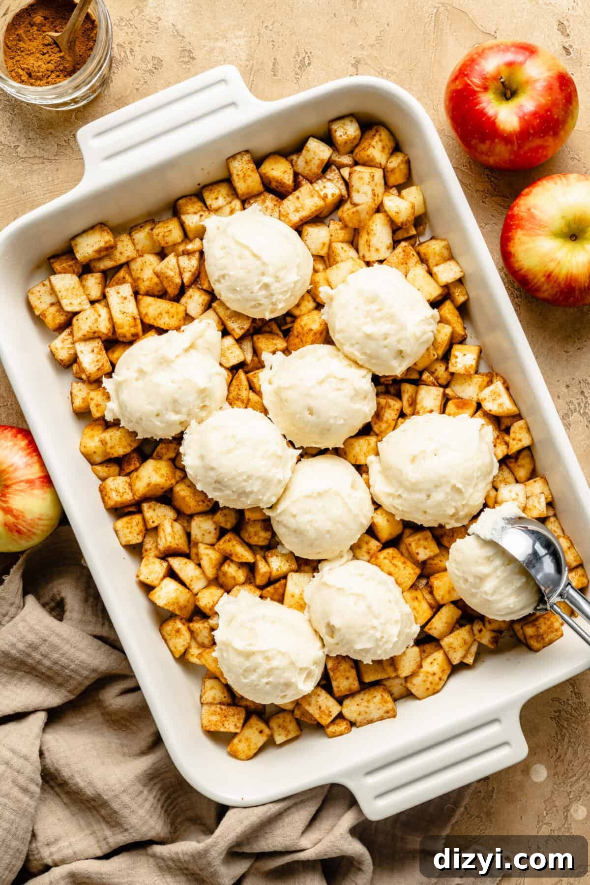 a white baking dish filled with chopped, spiced apples and scoops of vanilla icing
