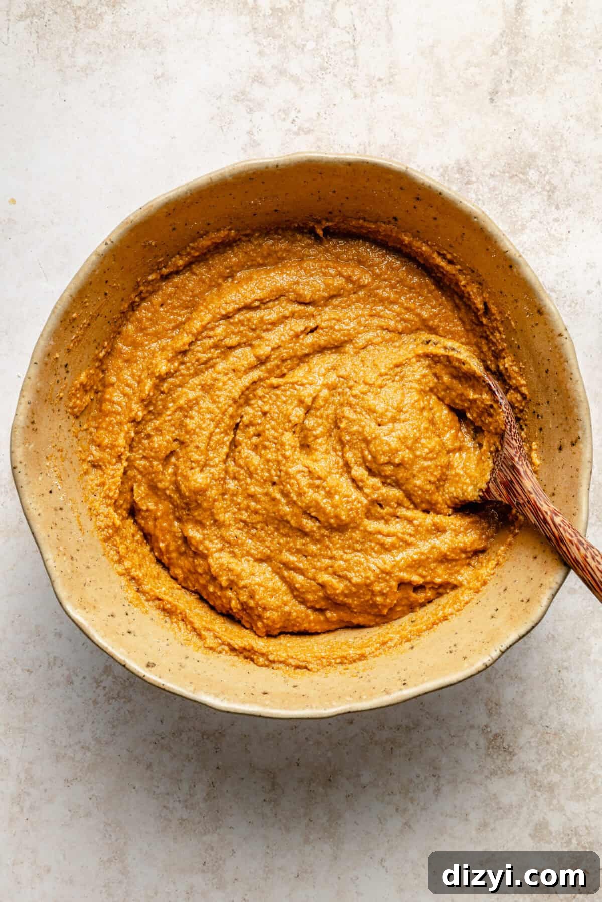 a large bowl with a wooden spoon of orange pumpkin muffin batter