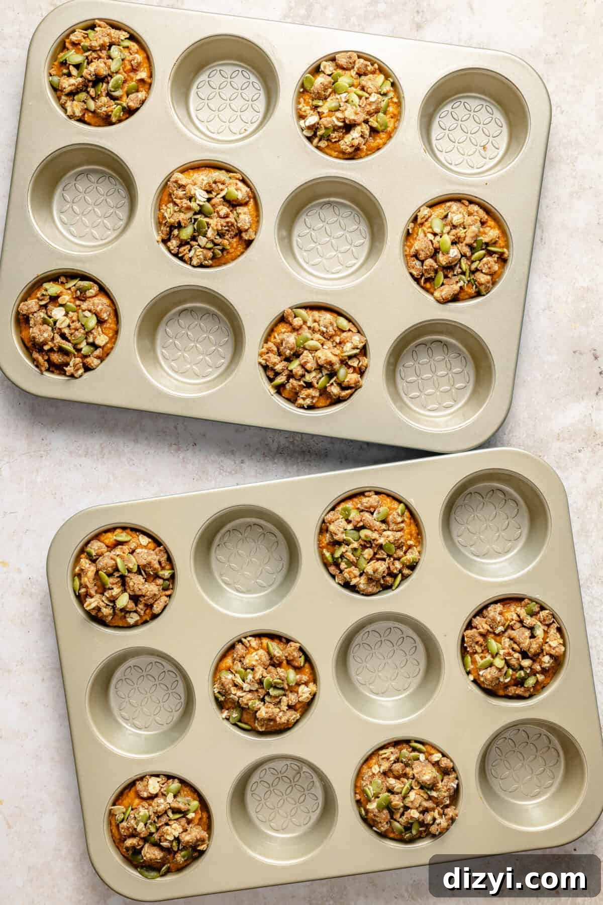 two muffin tins with pumpkin muffins topped with a streusel and pepitas topping