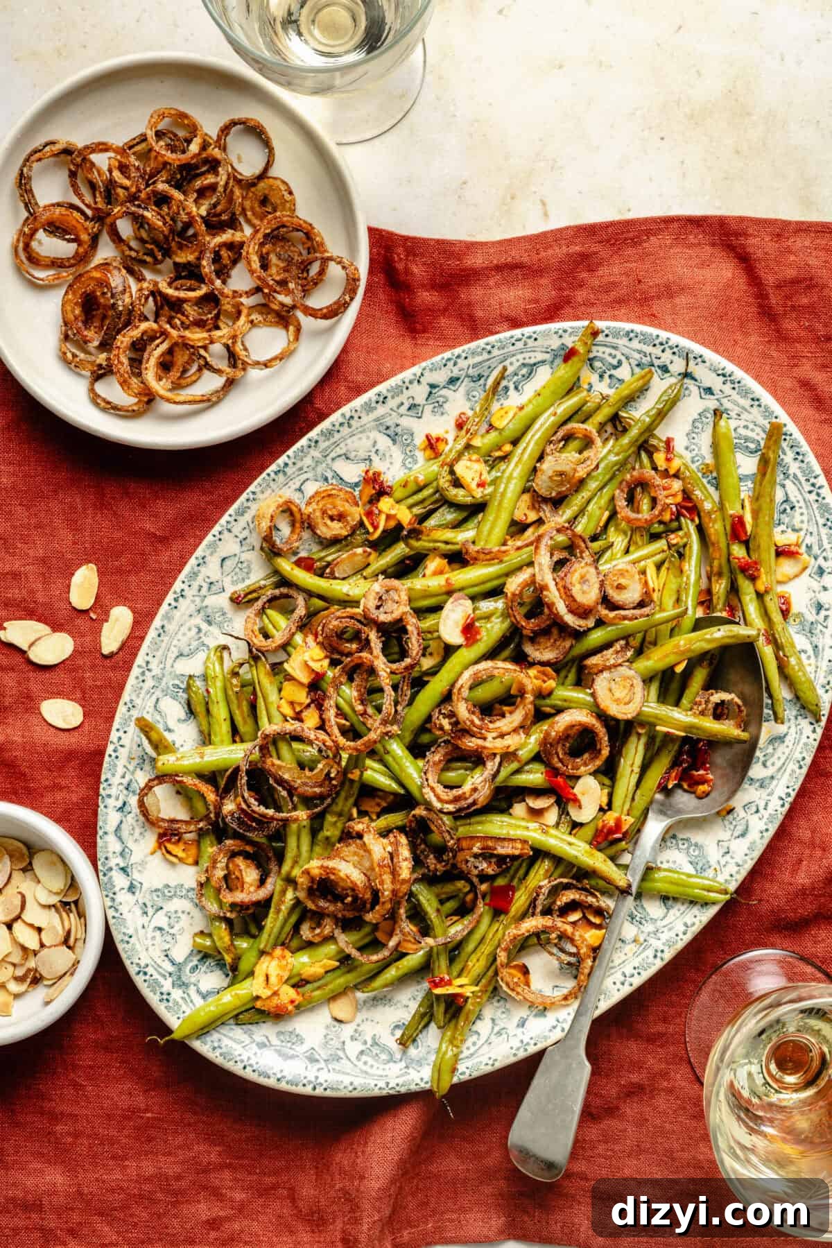 a large green toile platter with green beans, fried shallots, garlic, and calabrian chiles placed on a brick red linen napkin