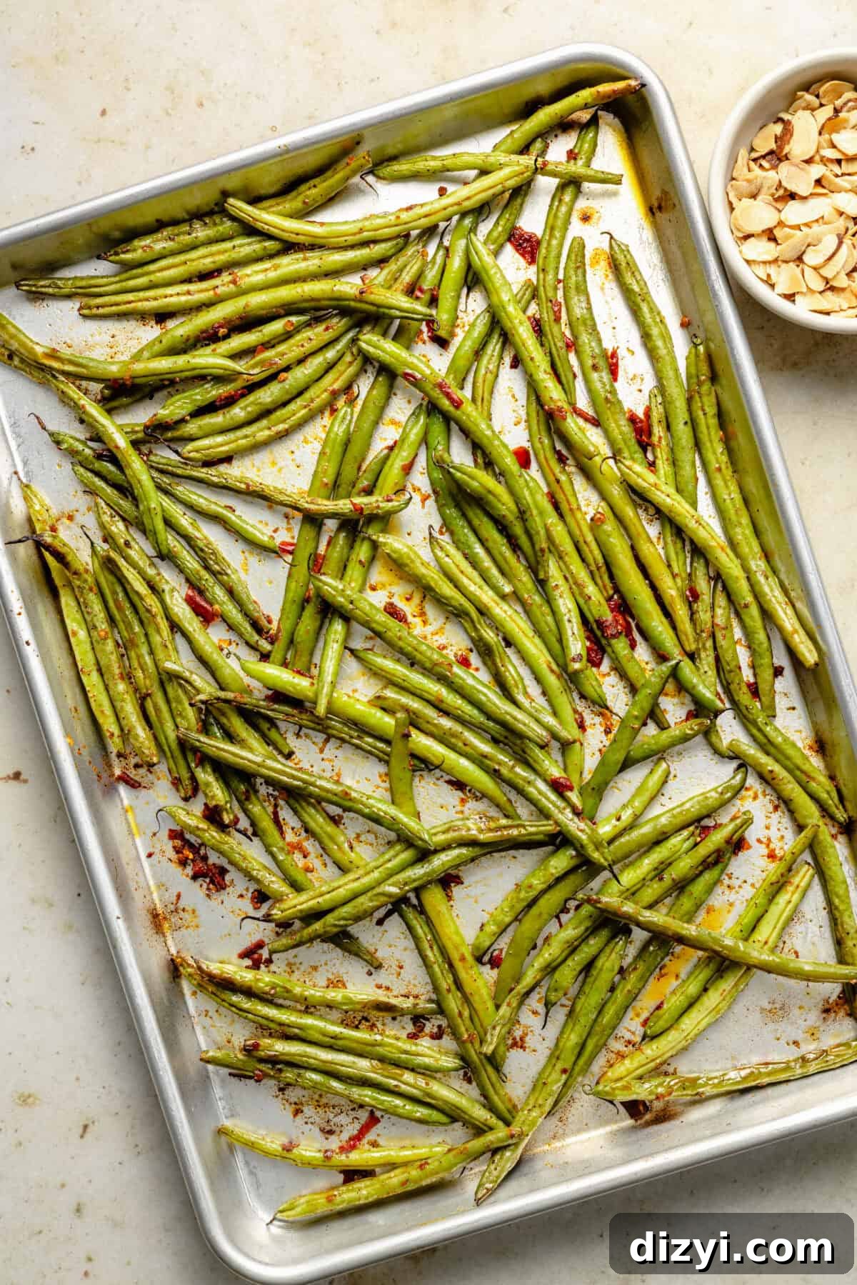 a large sheet pan with green beans and calabrian chiles; a small side bowl of slivered almonds