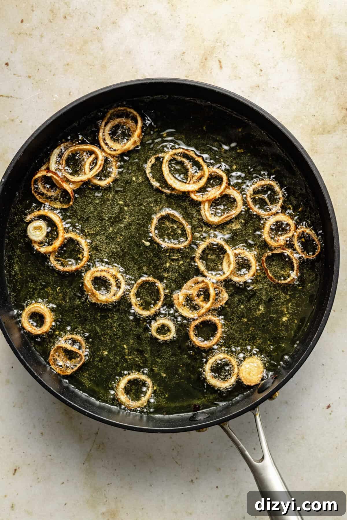 a large skillet with sizzling fried shallots on oil on a neutral background