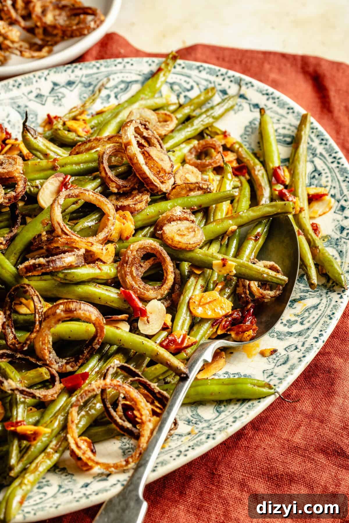 an up-close shot of green beans tossed with crispy shallots, garlic, and Calabrian chiles on a green toile platter