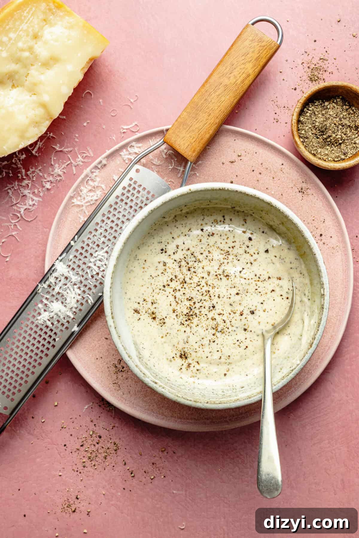 a bowl of creamy dressing with a microplane and Parmesan cheese