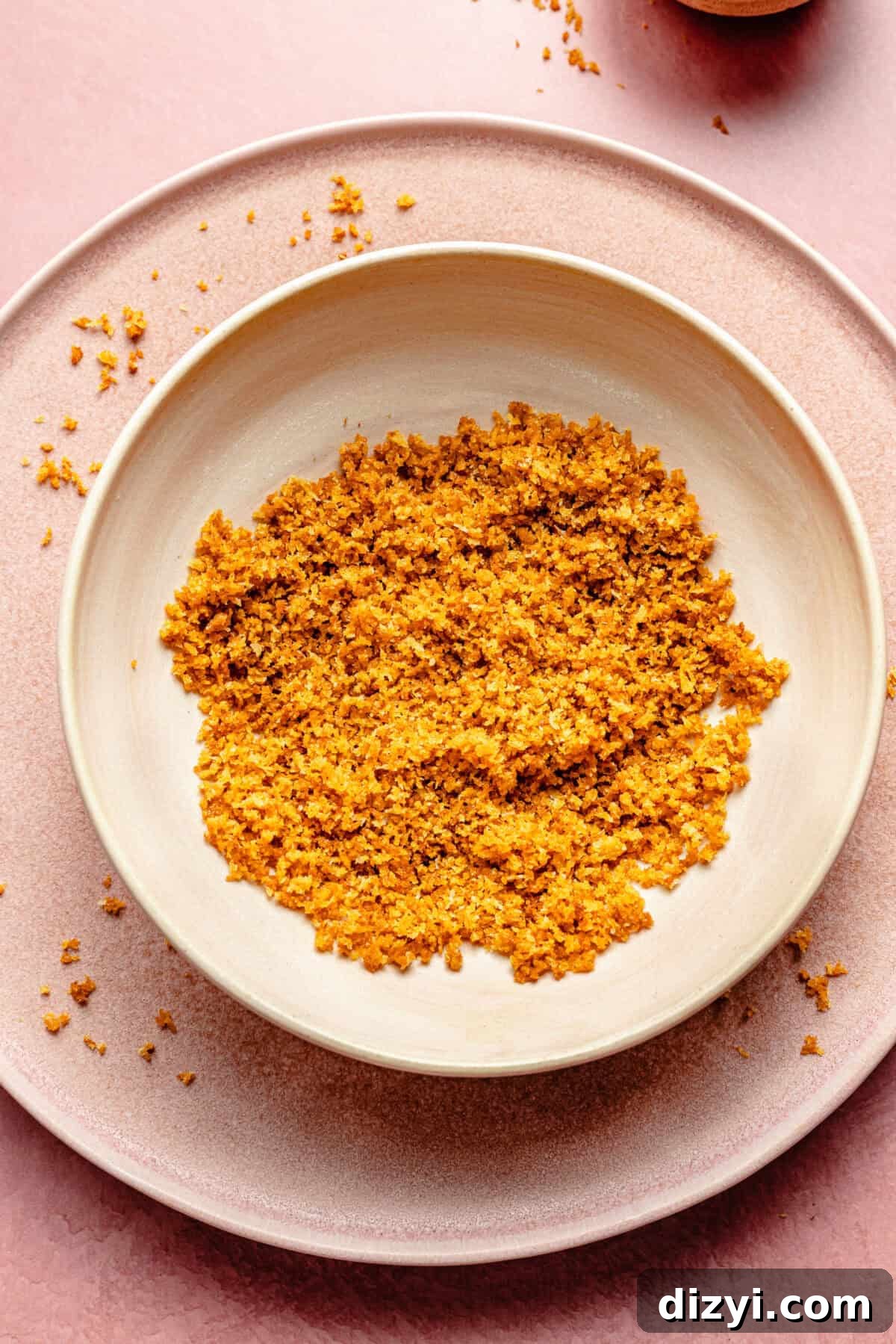 a white bowl with toasted breadcrumbs on a light pink background