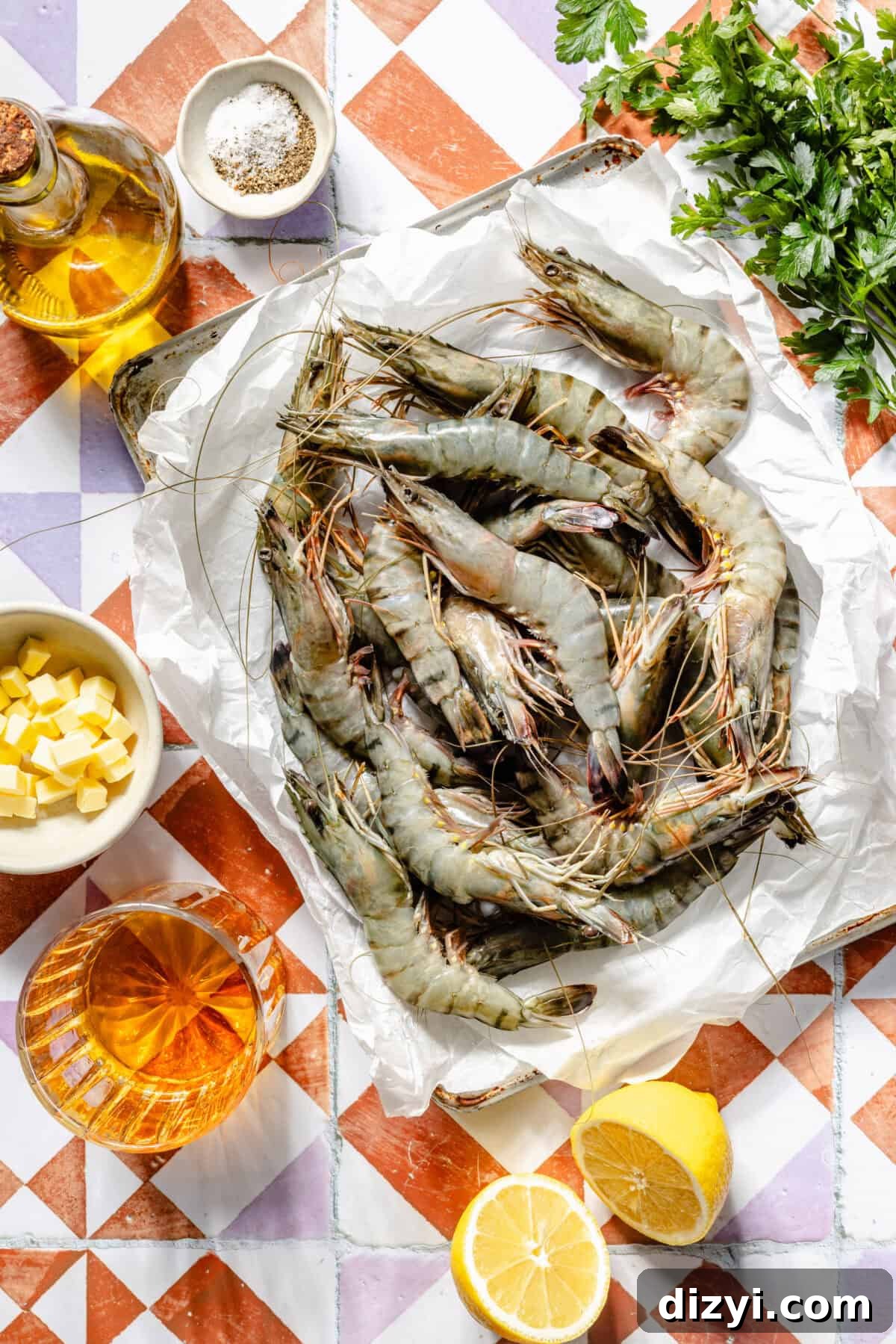 a flat-lay of ingredients including raw shrimp, butter, fresh parsley, lemon, olive oil, salt, and pepper