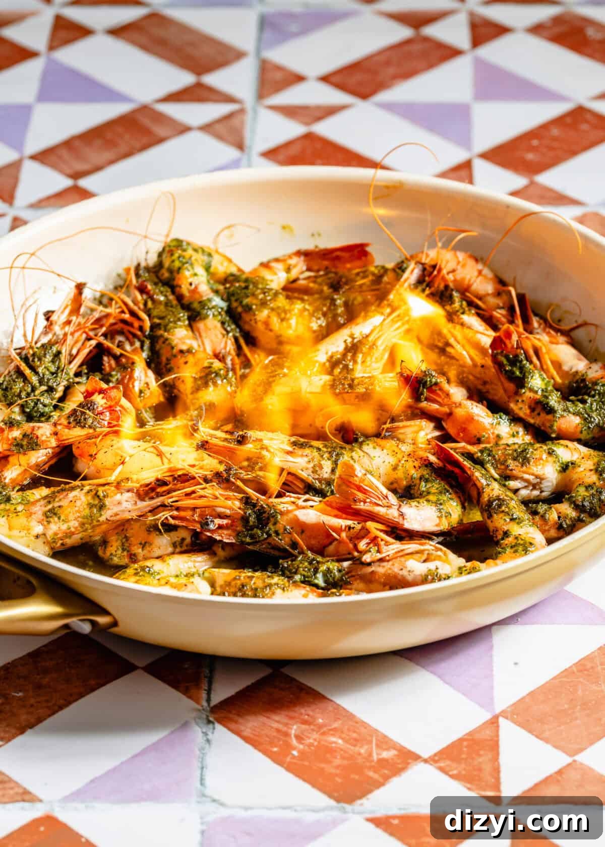 a white skillet with cooked shrimp tossed in parsley oil on an orange, white, and purple background