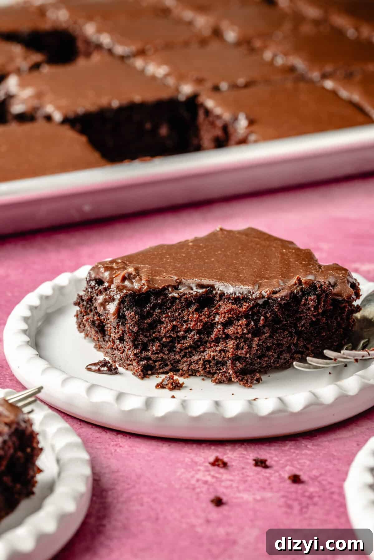 Kiki's Texas Chocolate Sheet Cake Recipe 6 a slice of partially eaten Texas sheet cake with chocolate frosting on a white plate and pink background
