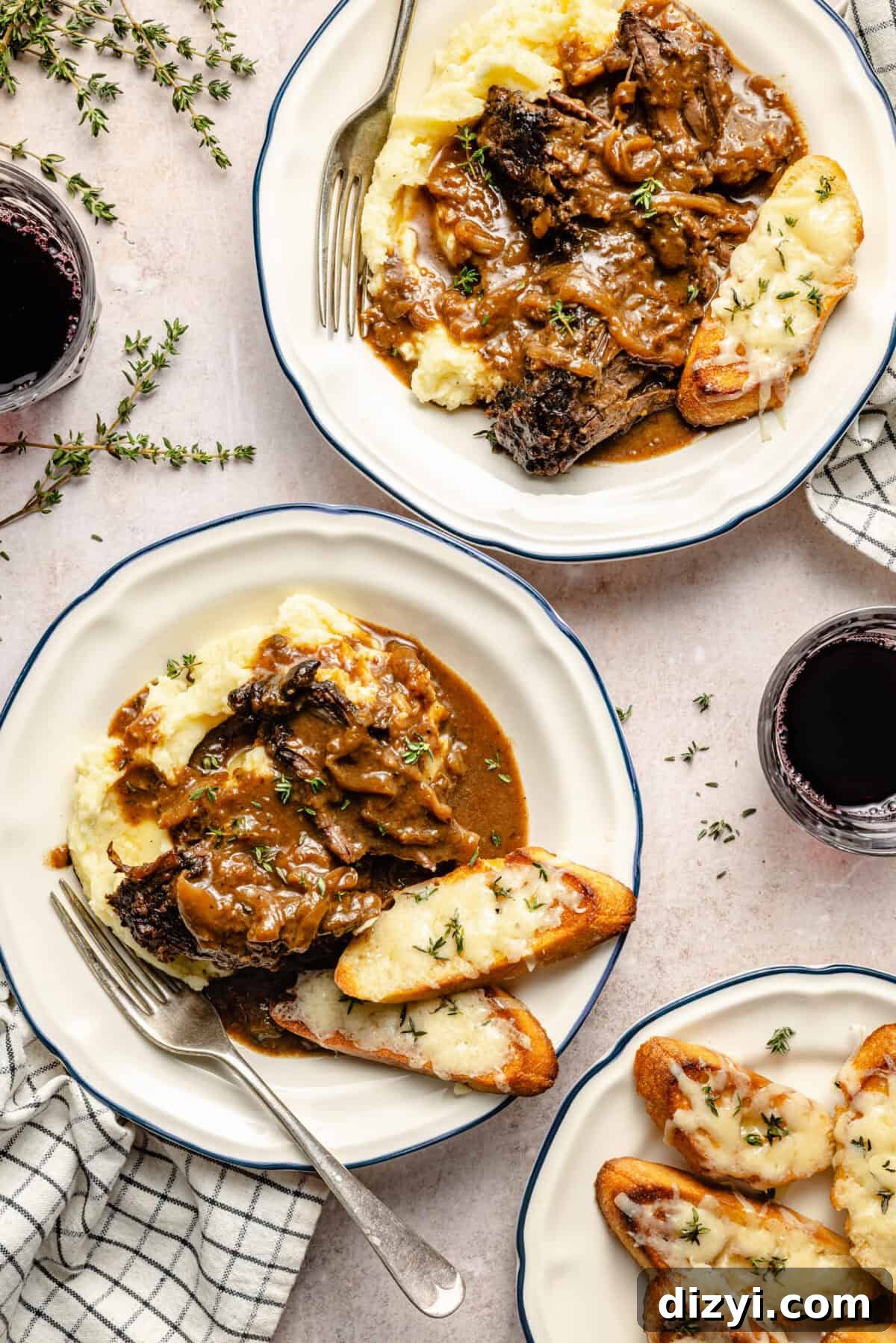 two plates with mashed potatoes, braised beef, and cheesy toasted garnished with fresh thyme on a neutral background