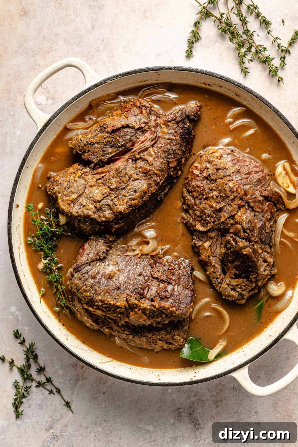 a large white Dutch oven with braised beef, sauce, and fresh herbs