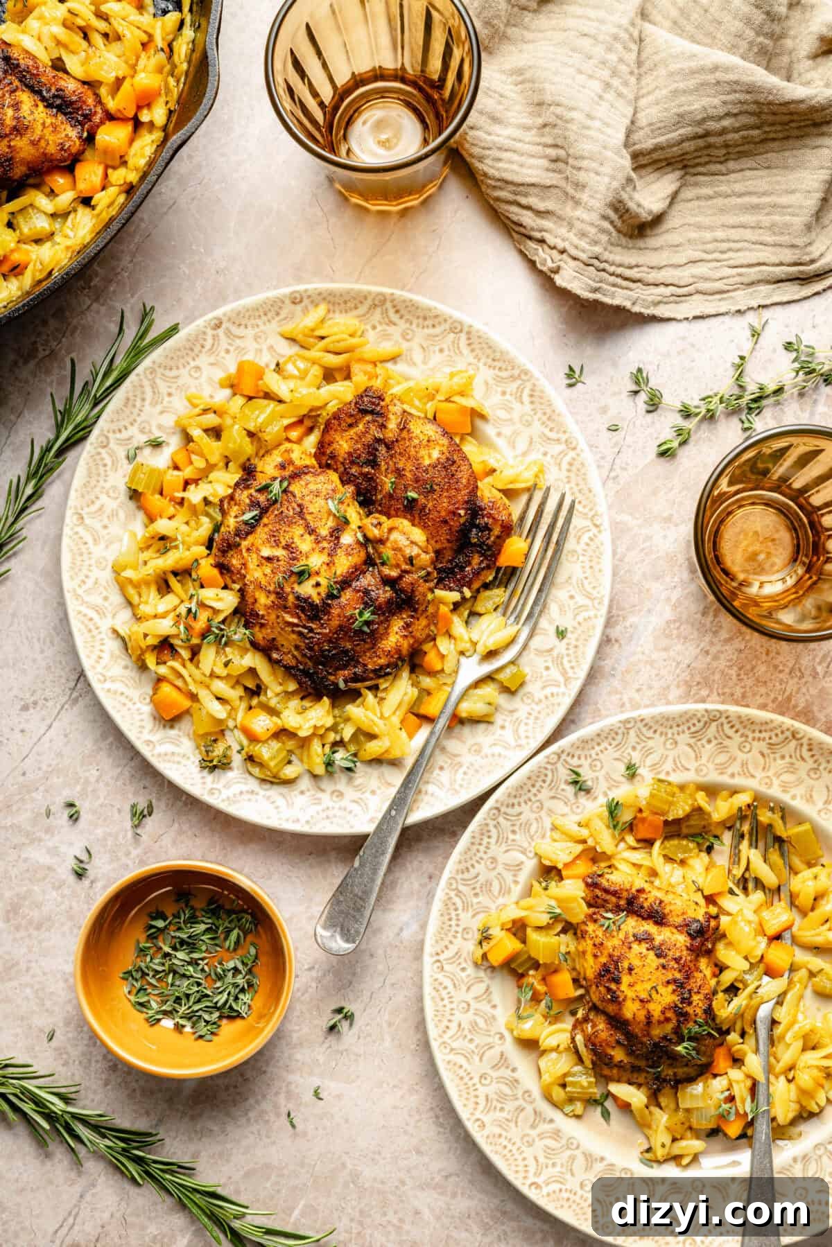 two plates with orzo, vegetables, seared chicken thighs, and fresh herbs on a neutral background