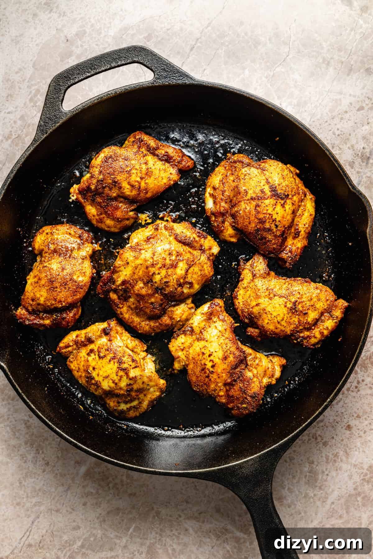 a cast-iron skillet with seared chicken thighs on a neutral background