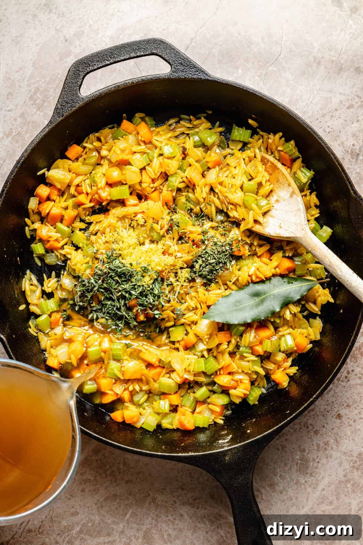 a cast-iron skillet with diced carrots, celery, orzo, and fresh herbs
