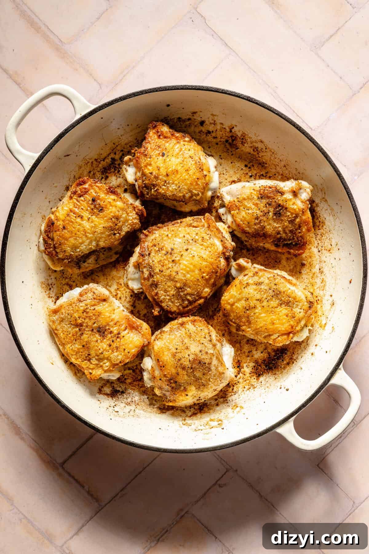 seared chicken thighs in a white Dutch oven on a light pink background